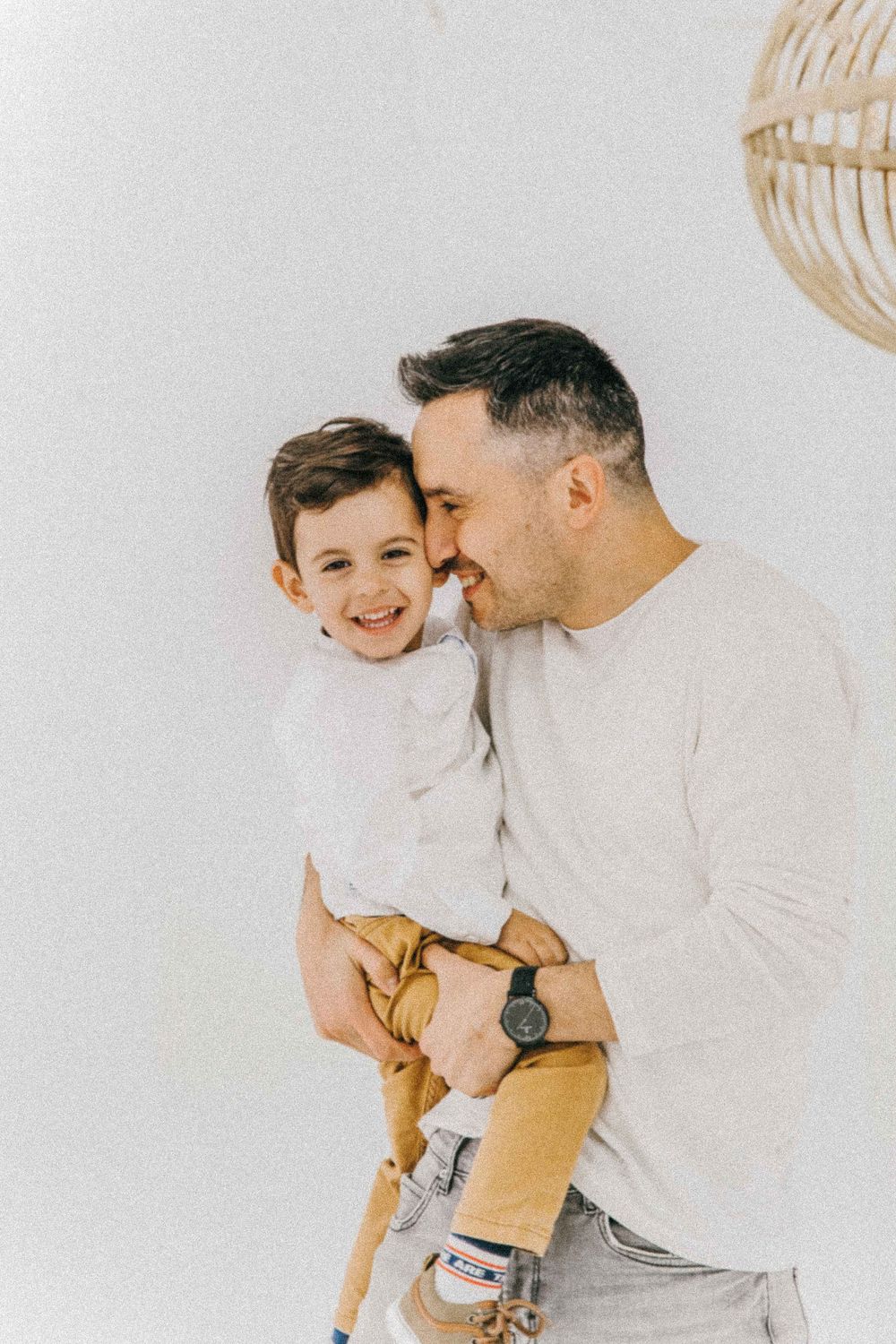 Father and child share joyful moments in casual white outfits. Create timeless memories with our maternity, newborn, and family photography