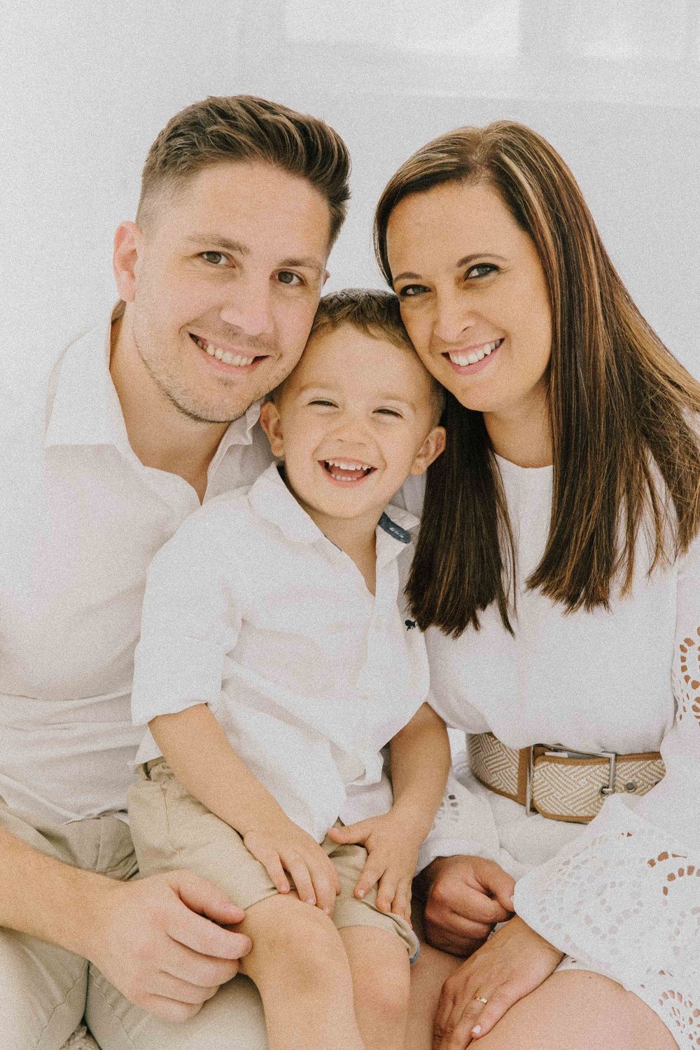 A cheerful family wearing white outfits poses together for a series of loving portraits. Alenquer, Lisbon, and Portugal photography studio.
