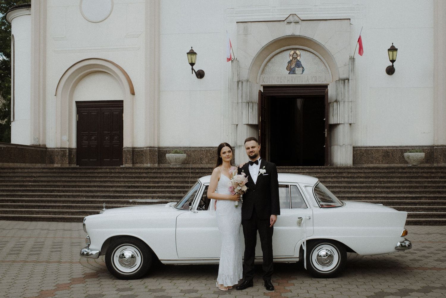 Classic white vintage car parked in front of elegant church building.