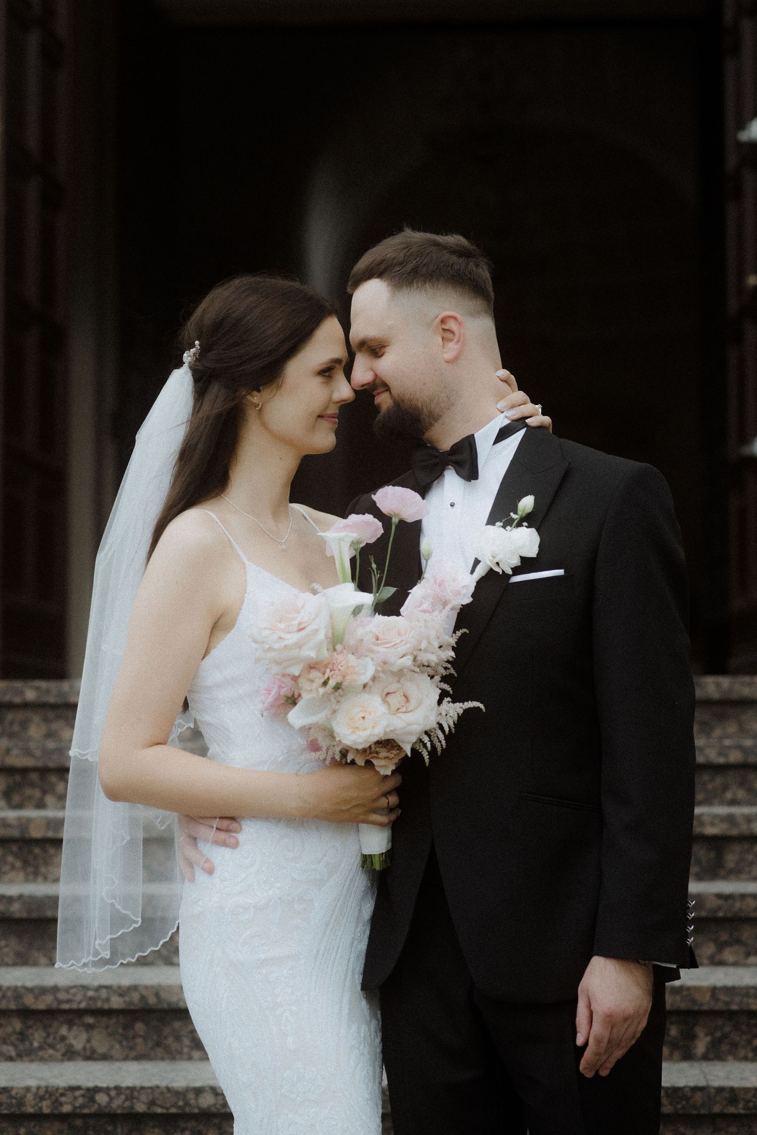 Intimate wedding portraits captured against dark background with bride holding pink bouquet.