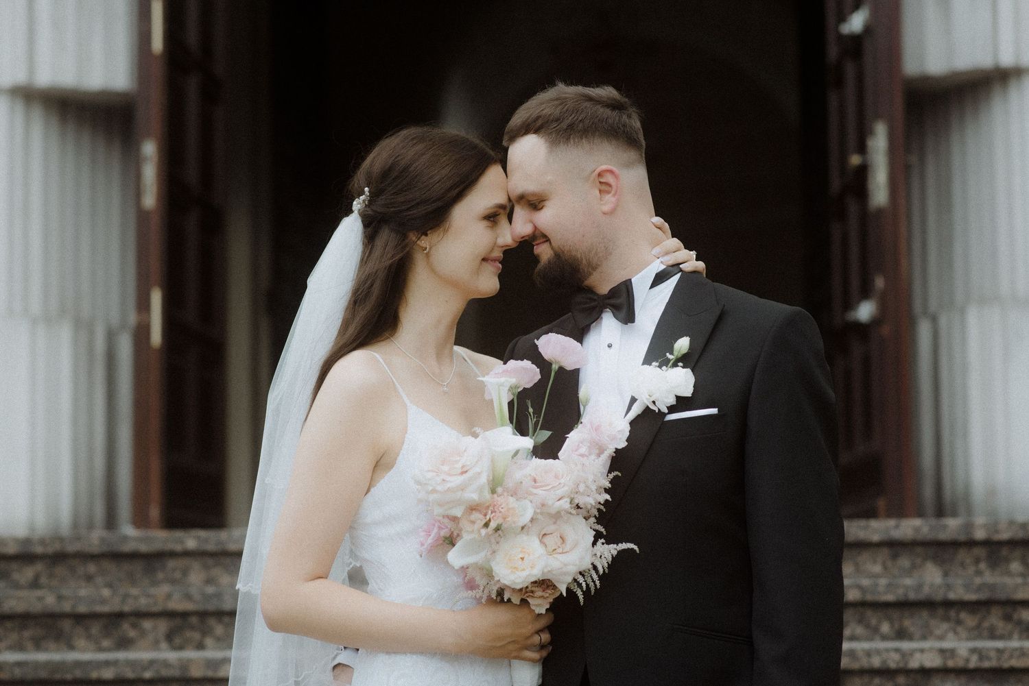 Couple sharing an intimate moment in front of white church entrance during a wedding ceremony.