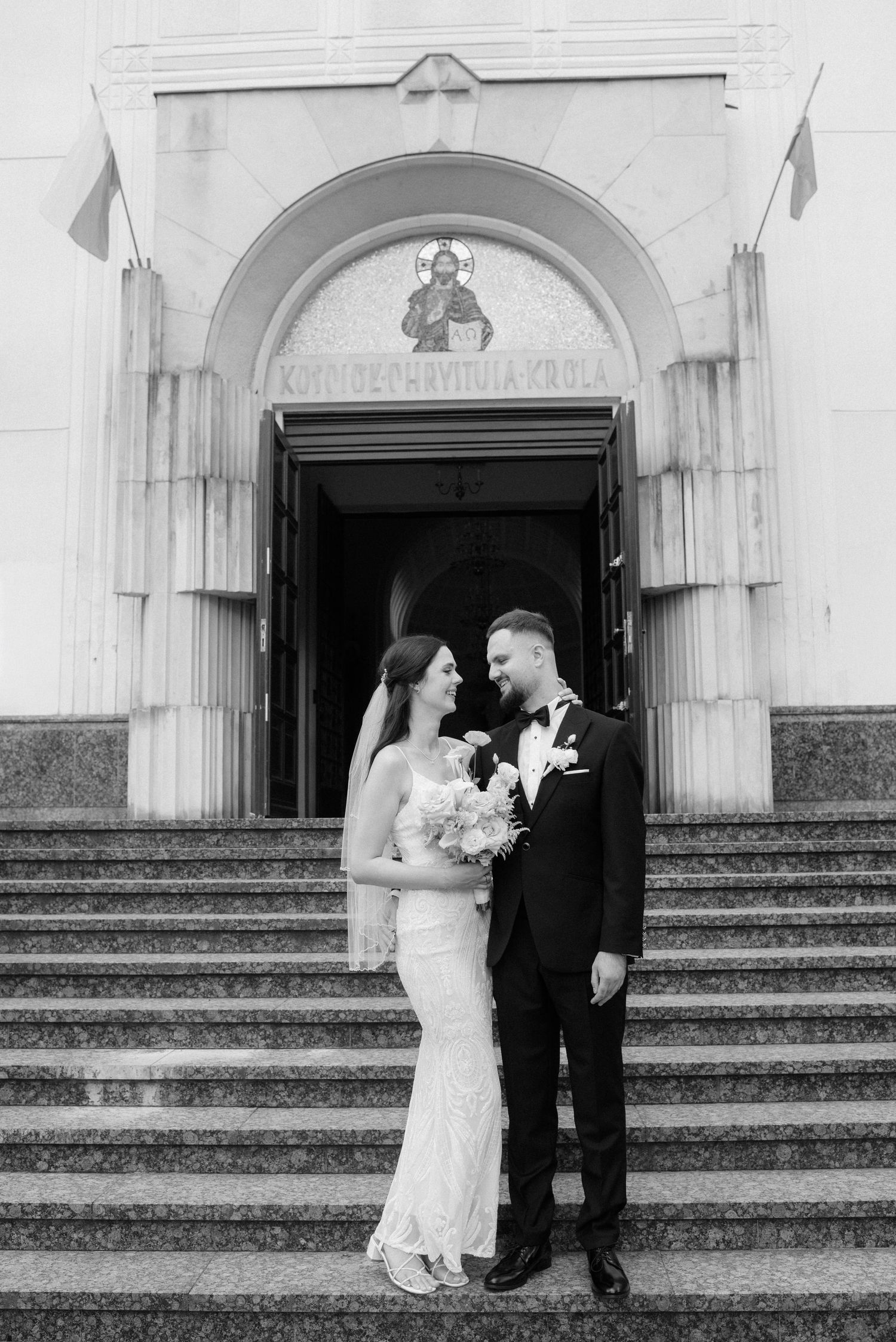 A couple shares a romantic moment on stone steps outside a grand church entrance.