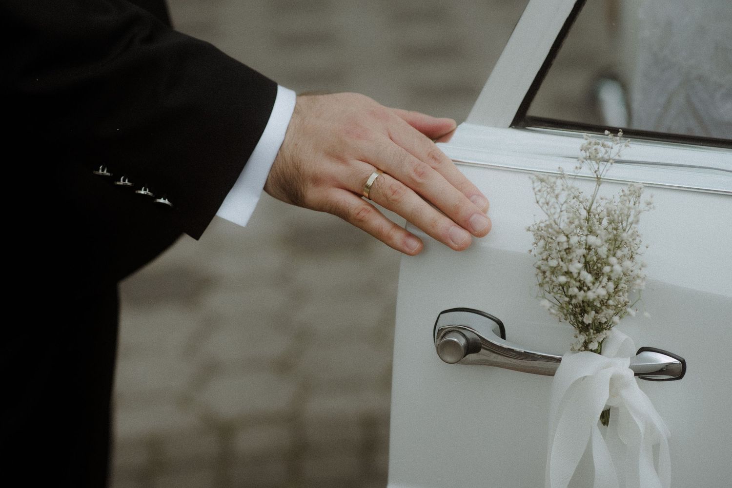 Wedding details with hands holding white floral arrangements and documents on a bright background.