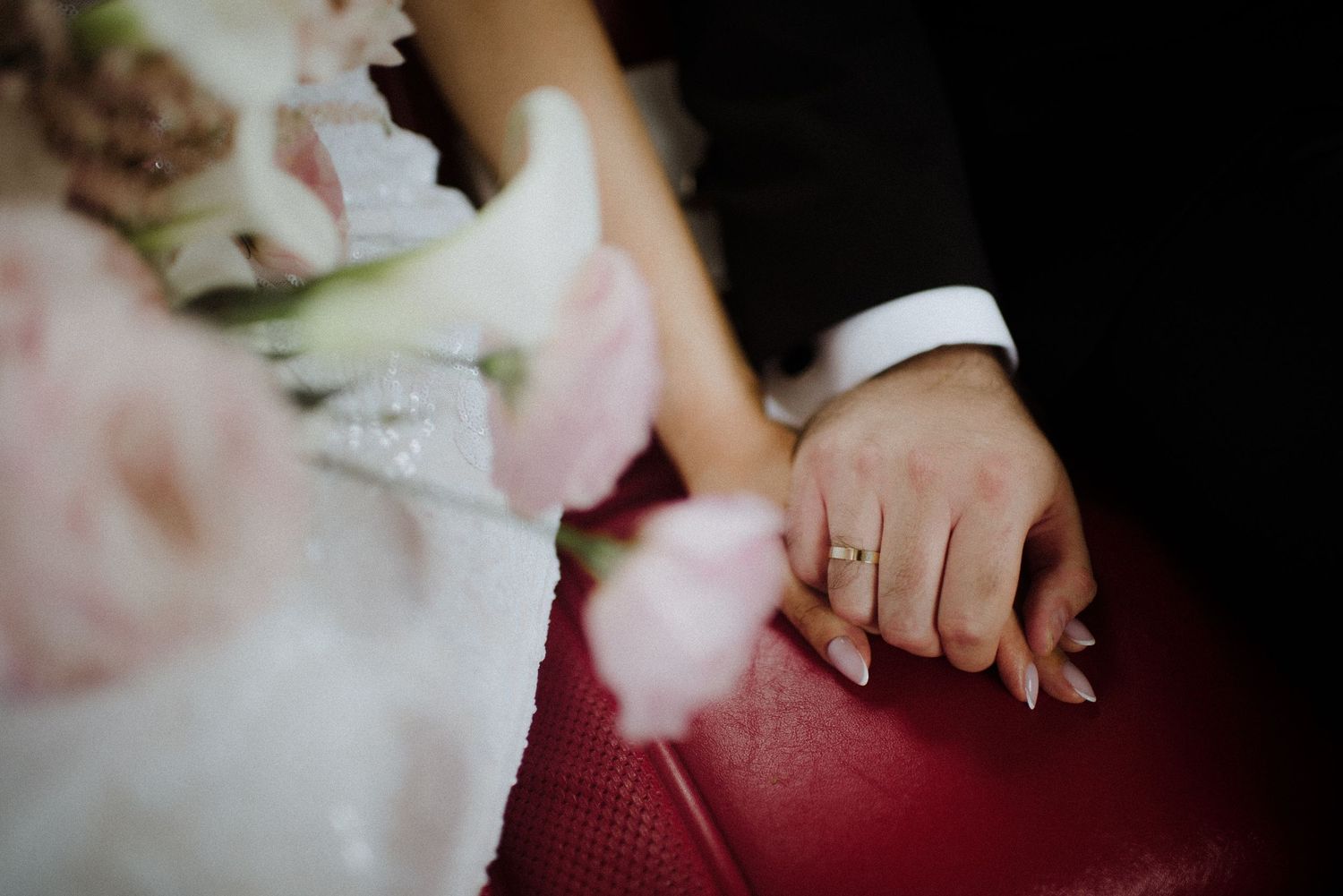 Close-up of hands with rings resting on a red surface in dim lighting.