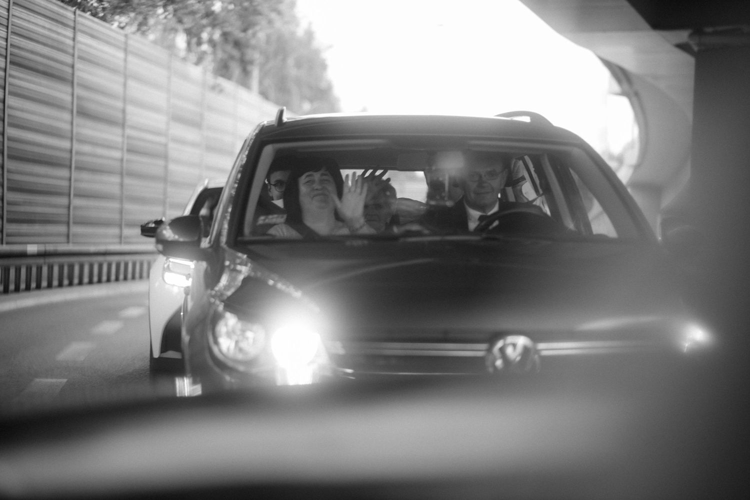 Black and white wedding car procession driving through sunlit streets.