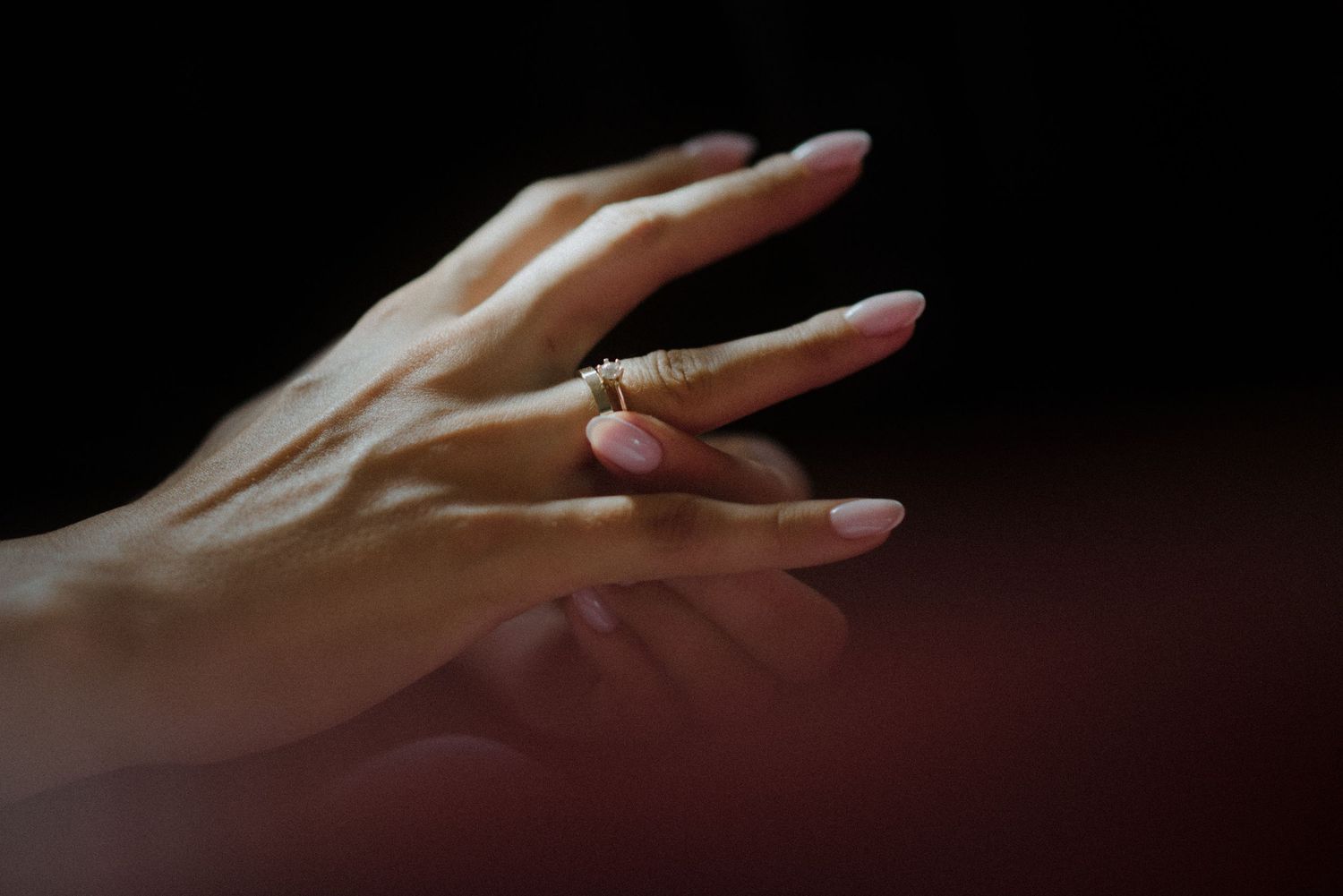 An elegant hand with a wedding band reaching across a dark background.