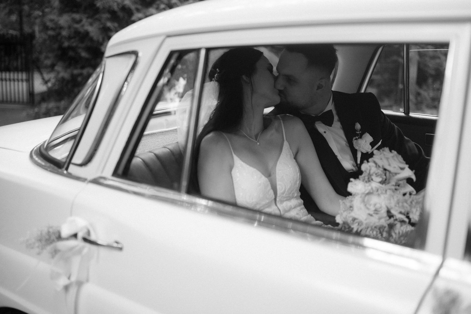 Classic vintage white car with couple inside dressed in wedding attire.