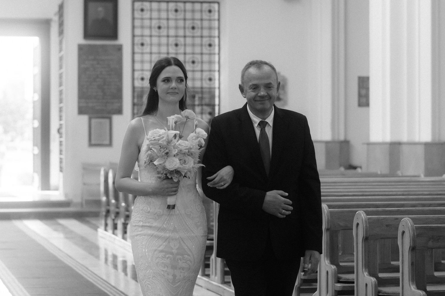 A bride walks down the church aisle accompanied by a family member during an elegant wedding ceremony.