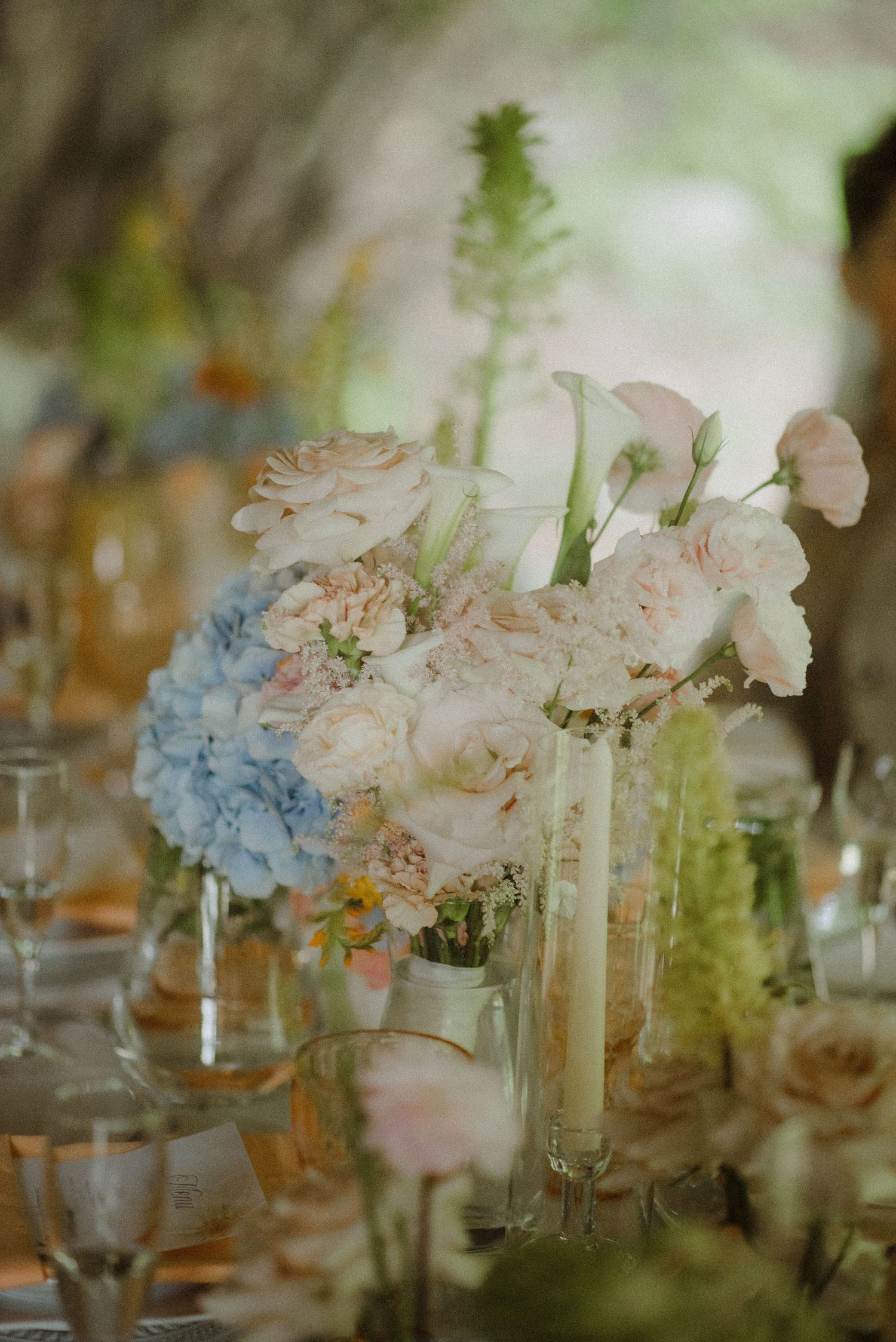 Romantic wedding reception centerpieces with pink and blue flowers in glass vases.
