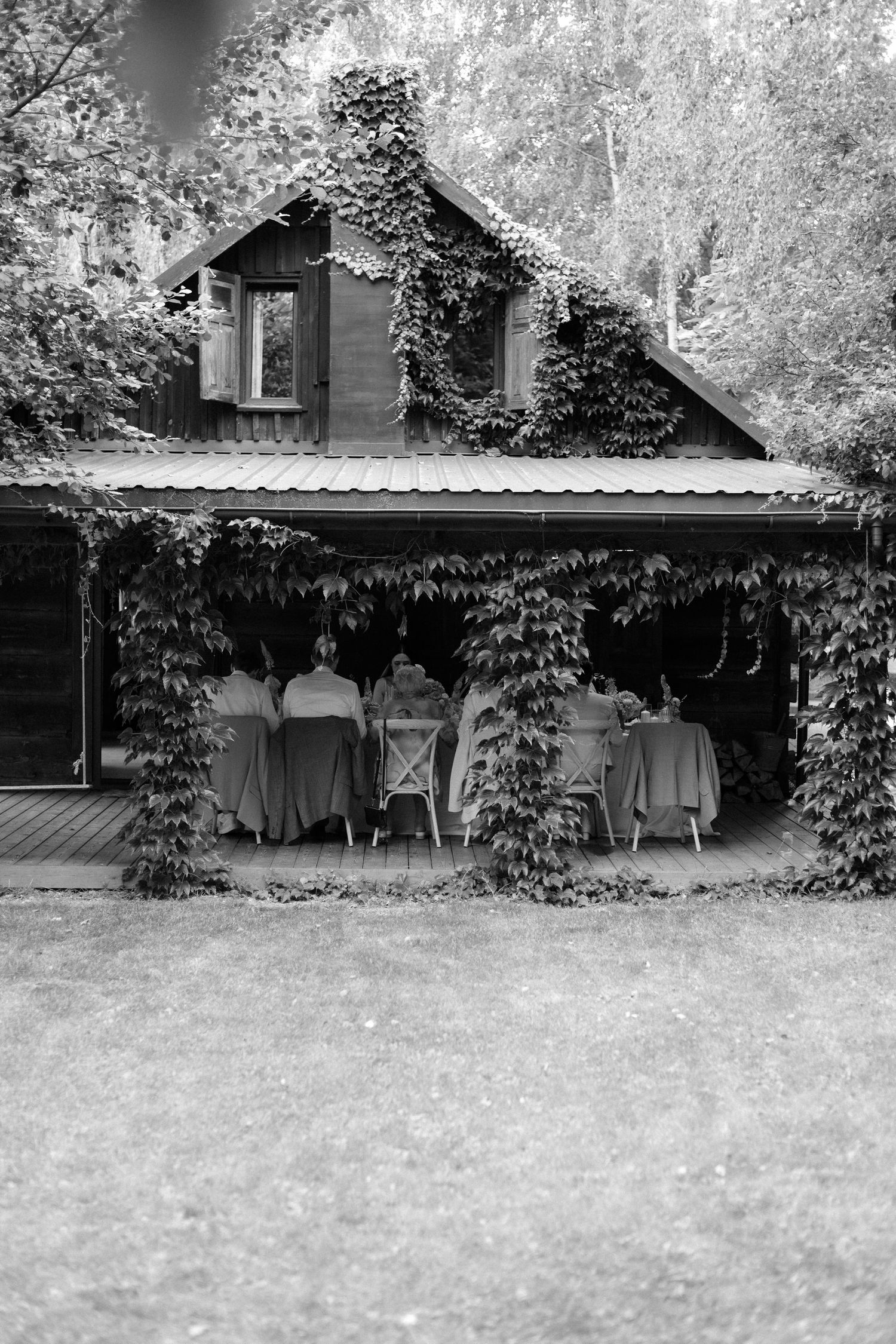 Black and white landscape view of a rural house with vine-covered walls and trees in the background.