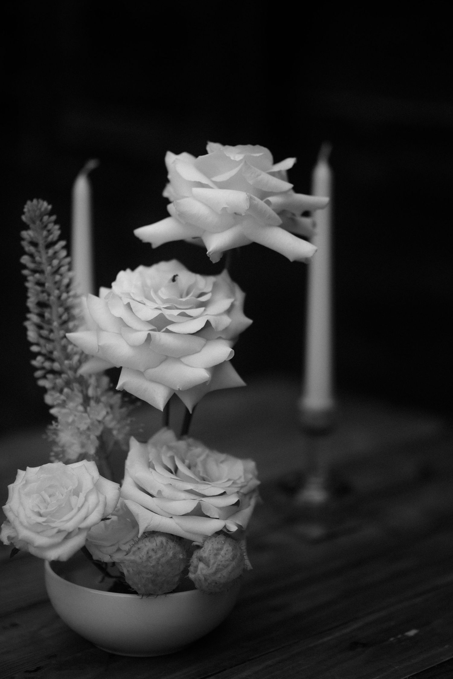 Elegant white roses and flowers arranged in a small bowl with candlesticks in black and white.