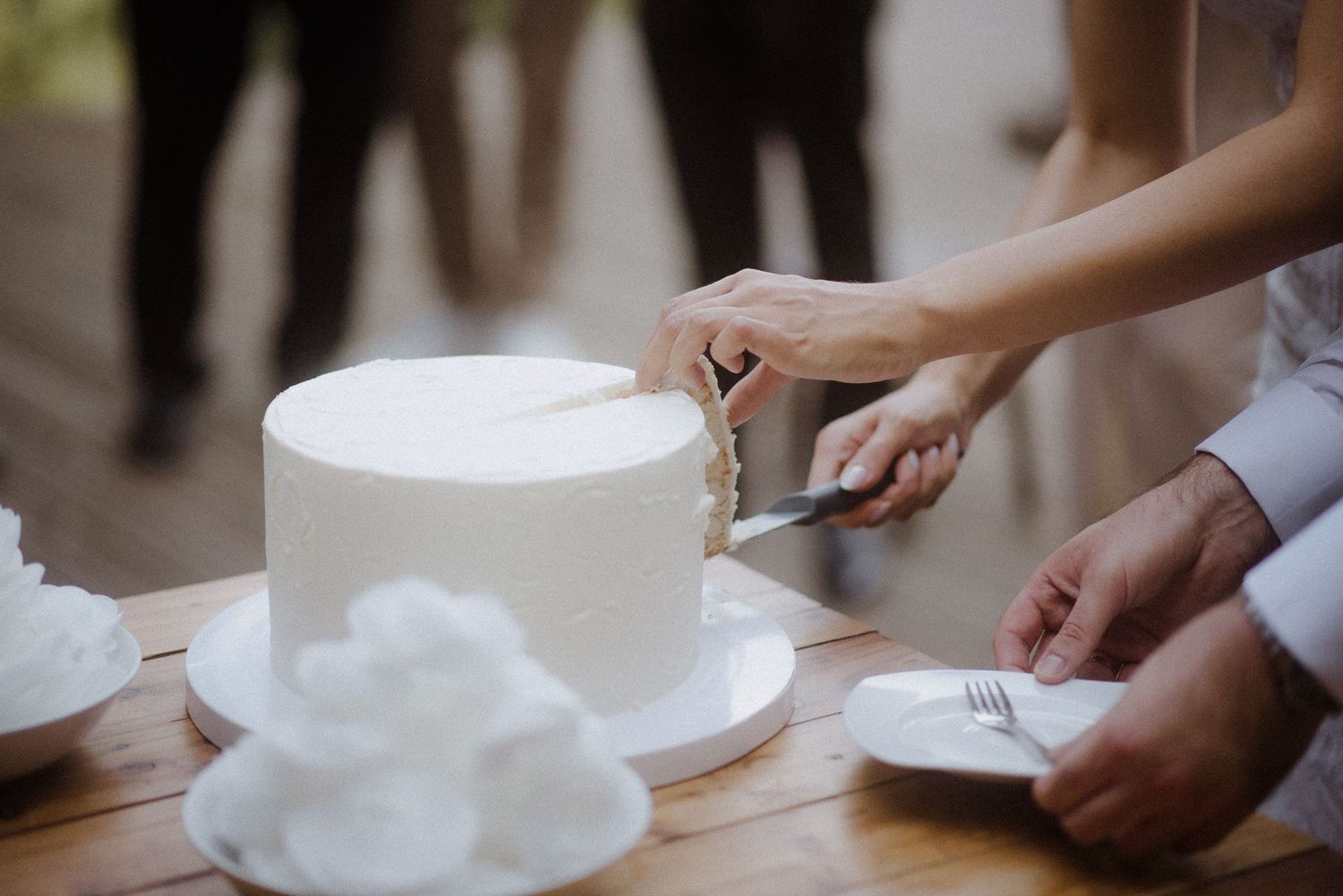 Wedding guests gather around a white wedding cake on display at an elegant reception.