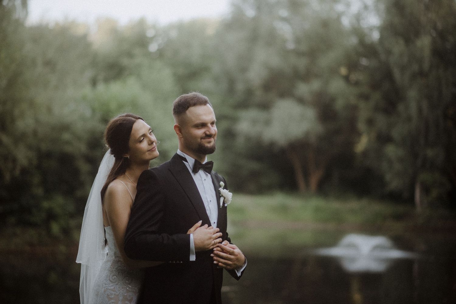 A romantic wedding photo taken outdoors with dreamy sunlit trees in the background.