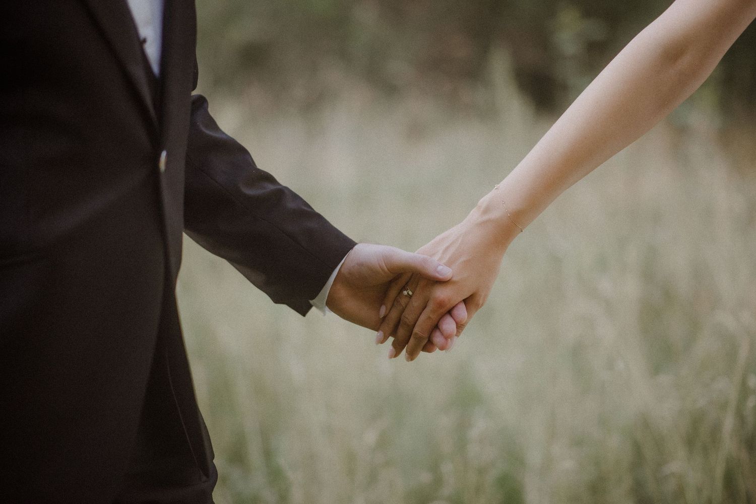 Close-up of hands reaching toward each other against a soft outdoor background.