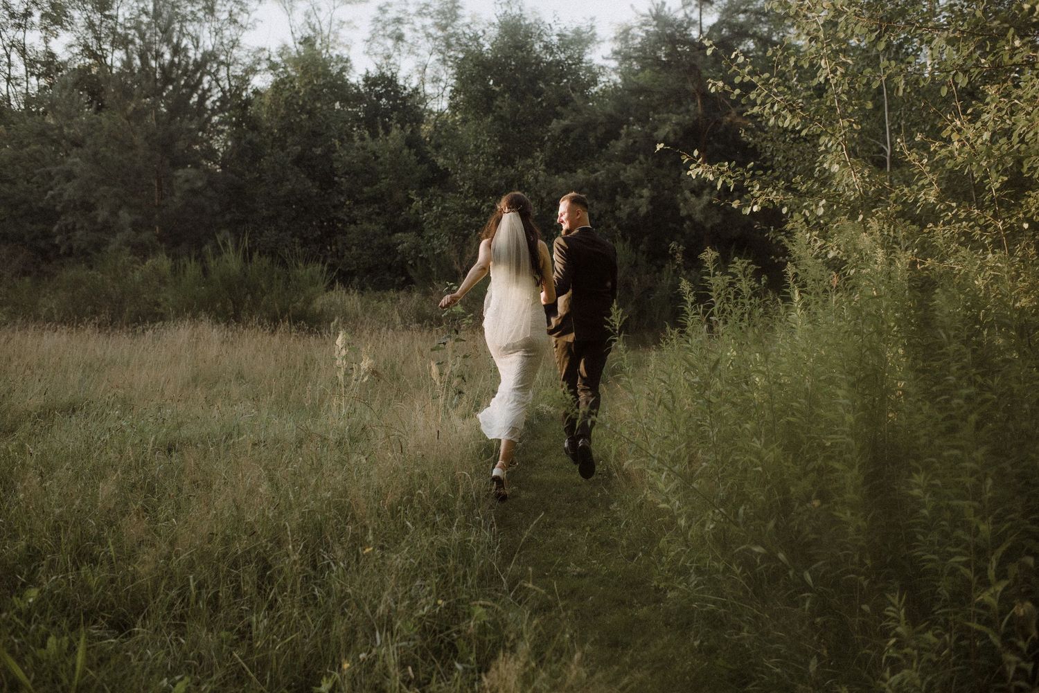 Wedding couple walking through tall grass in golden afternoon light.