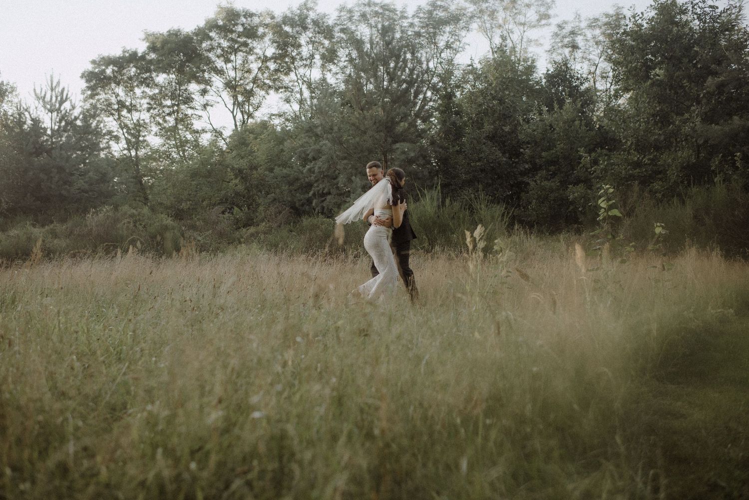 Person in a flowy white dress walking through a serene meadow at golden hour.