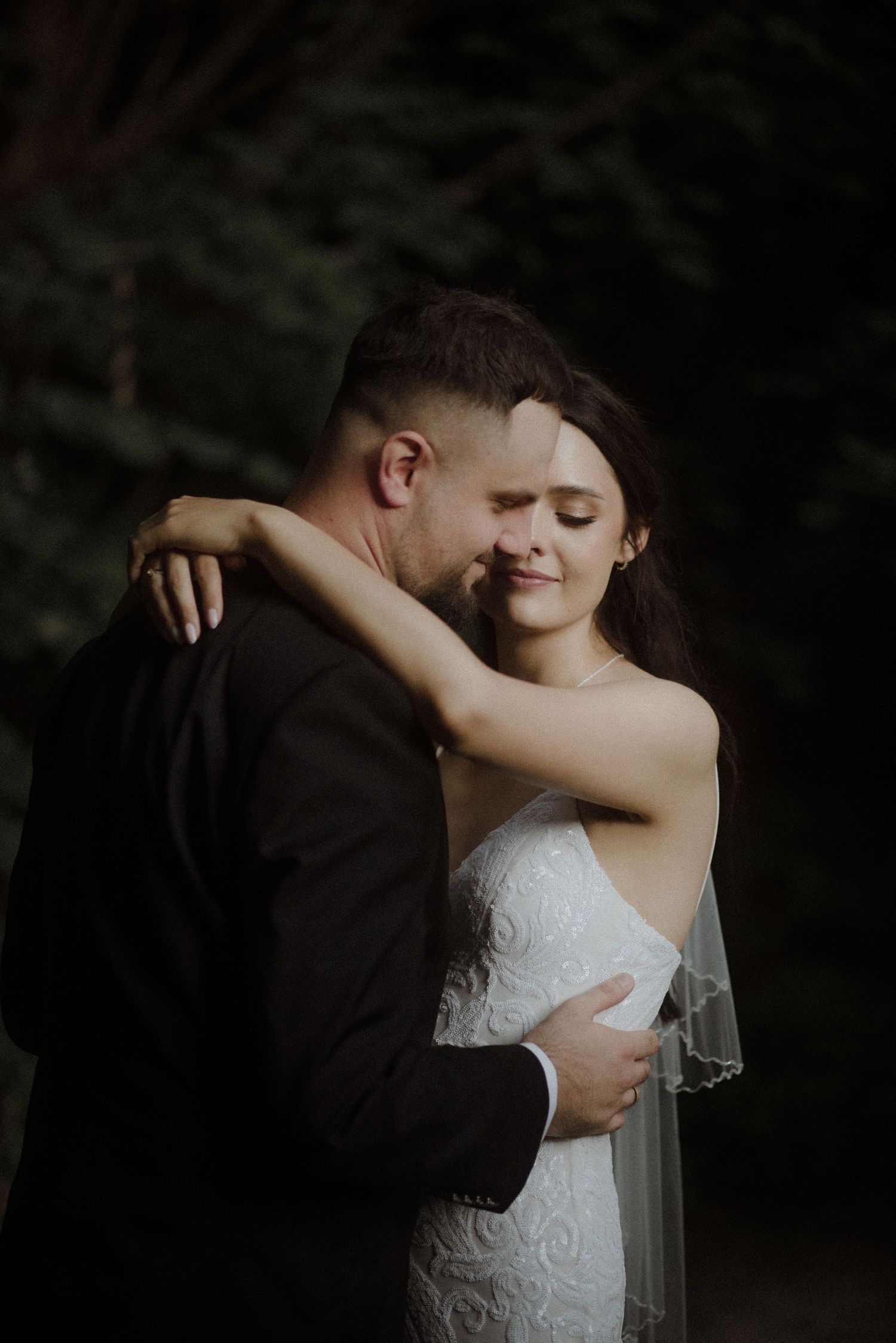 Intimate embrace captured in moody forest setting during wedding photoshoot.