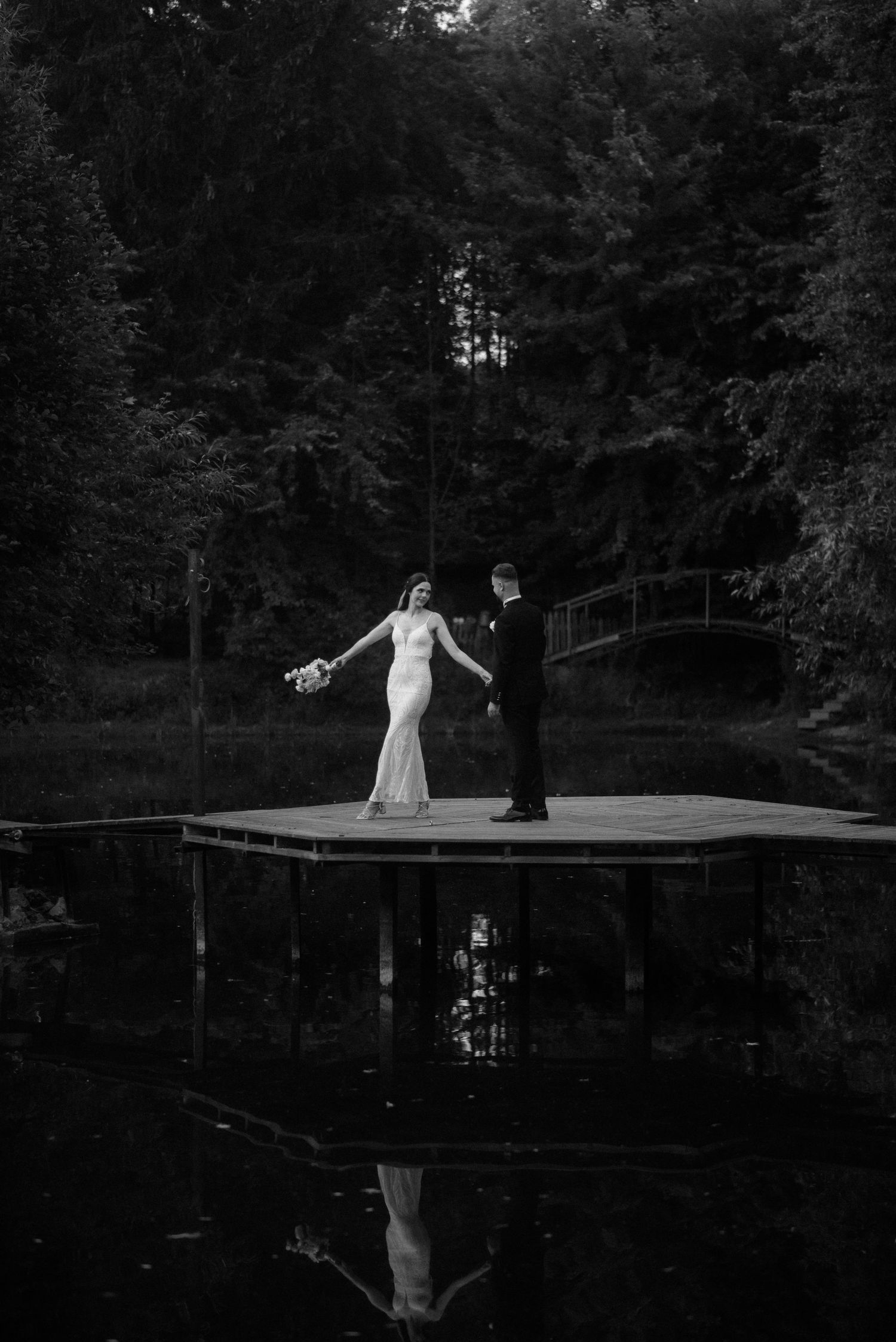 Silhouettes dancing on wooden dock over reflective lake at dusk.