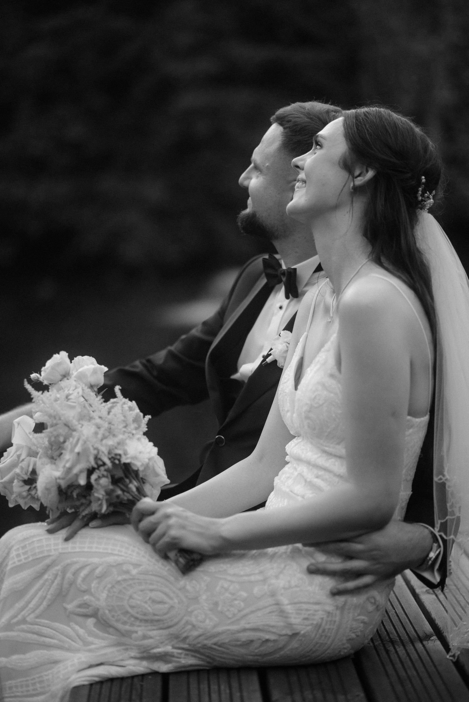 Two wedding guests seated on a dock by the water enjoying a moment together in black and white.
