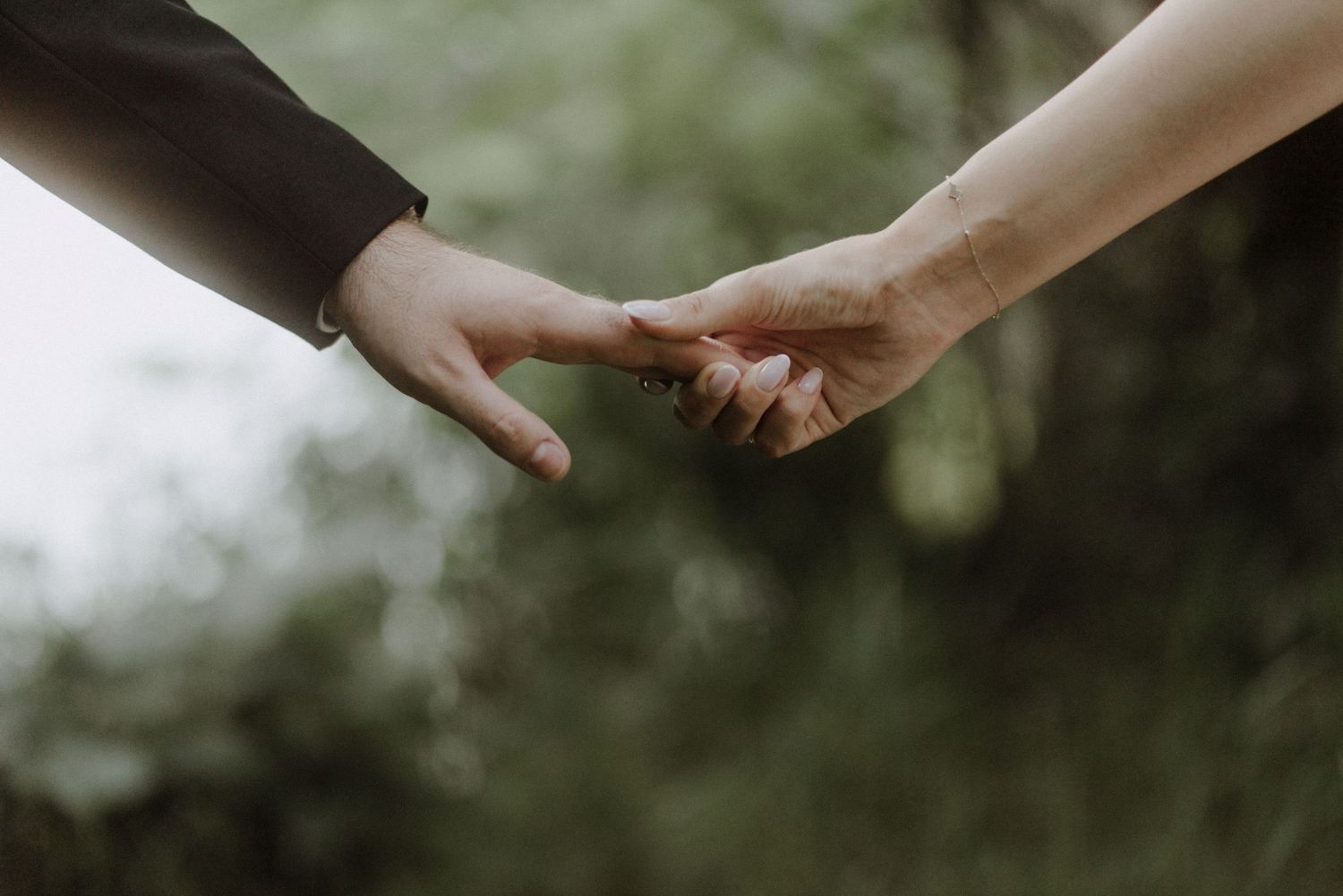 Close-up shot of hands reaching towards each other against a blurred natural background.