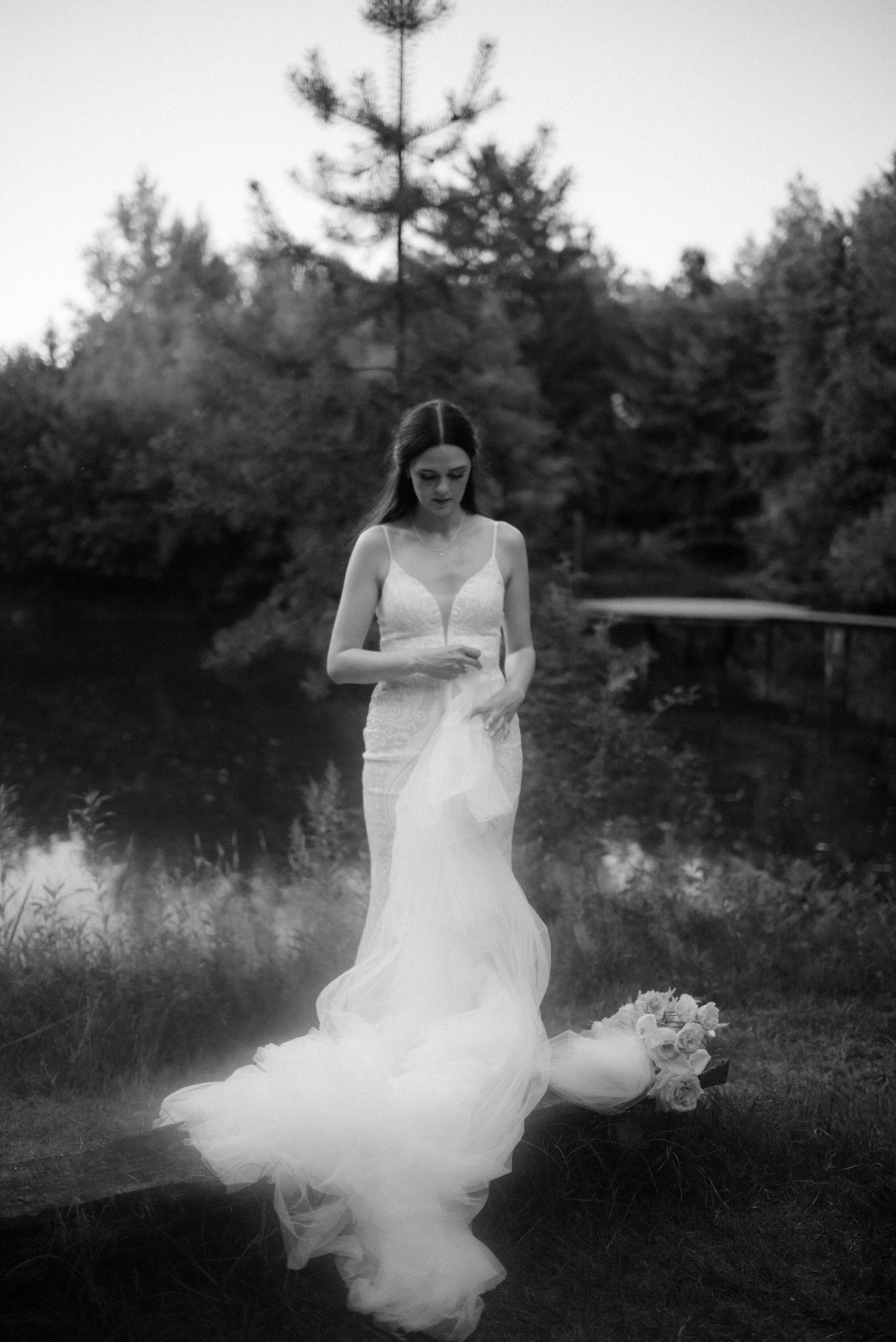 Ethereal black and white photos of someone in a white dress seated among pine trees.