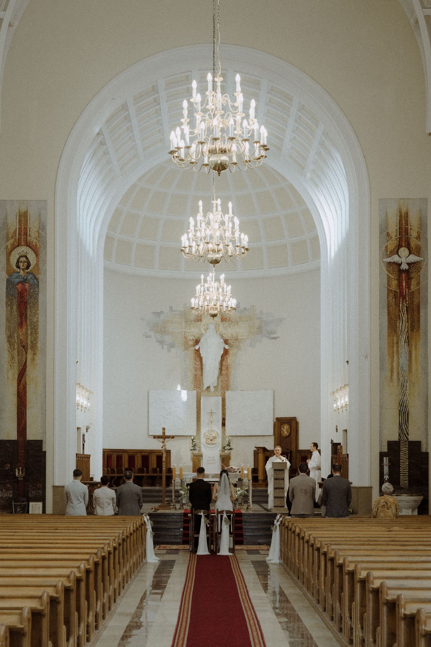Interior of a church with elegant crystal chandeliers, wooden pews, and a central aisle leading to an ornate altar.