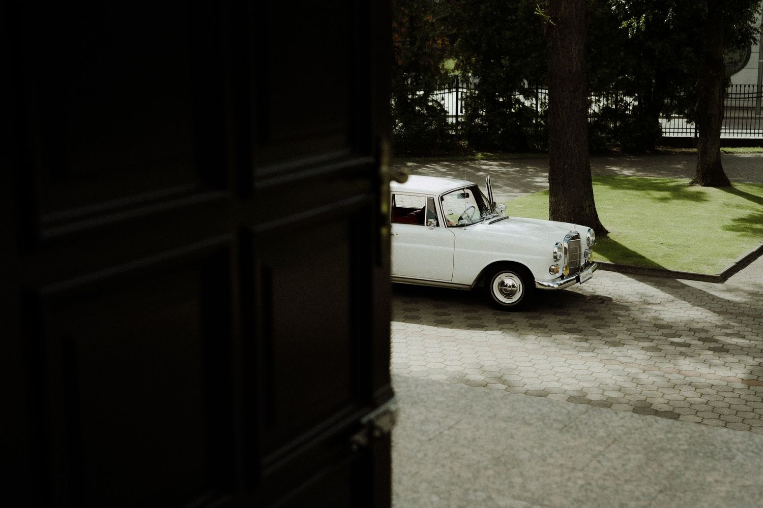 Black and white vintage car parked on a tree-lined residential street.