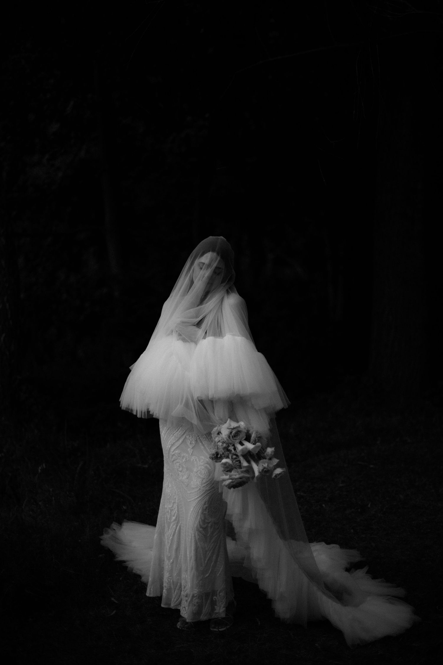 Dramatic black and white photo of a bride in a lace gown with flowing veil.