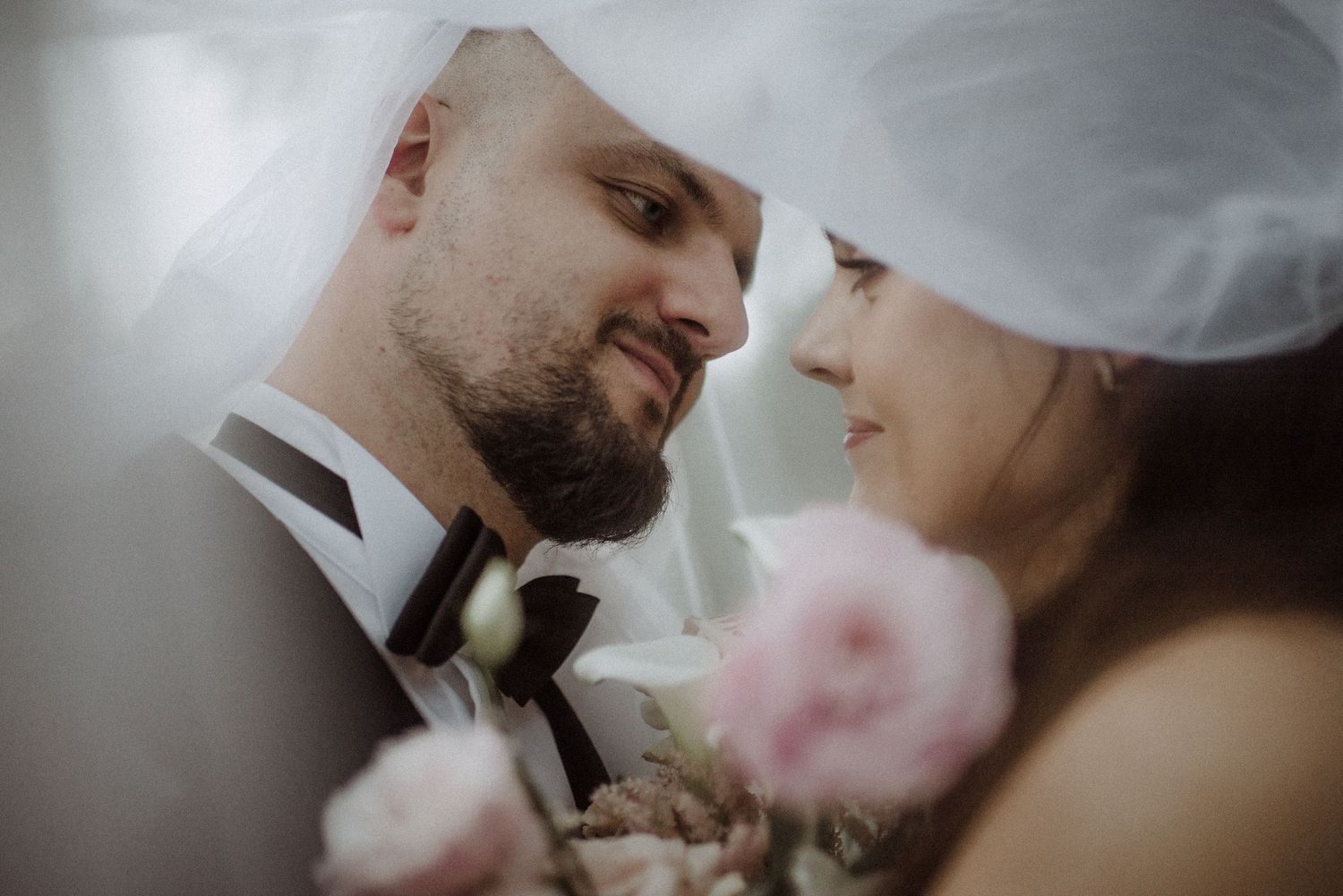 Intimate black and white portrait of newlyweds sharing a tender moment under a veil.