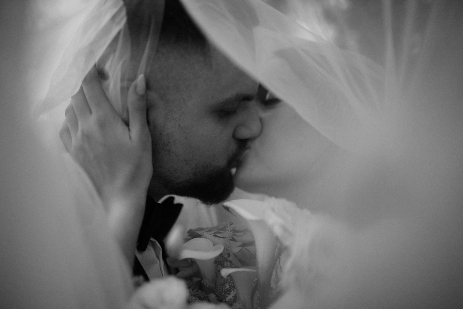 Intimate black and white wedding moment captured through delicate veil fabric.