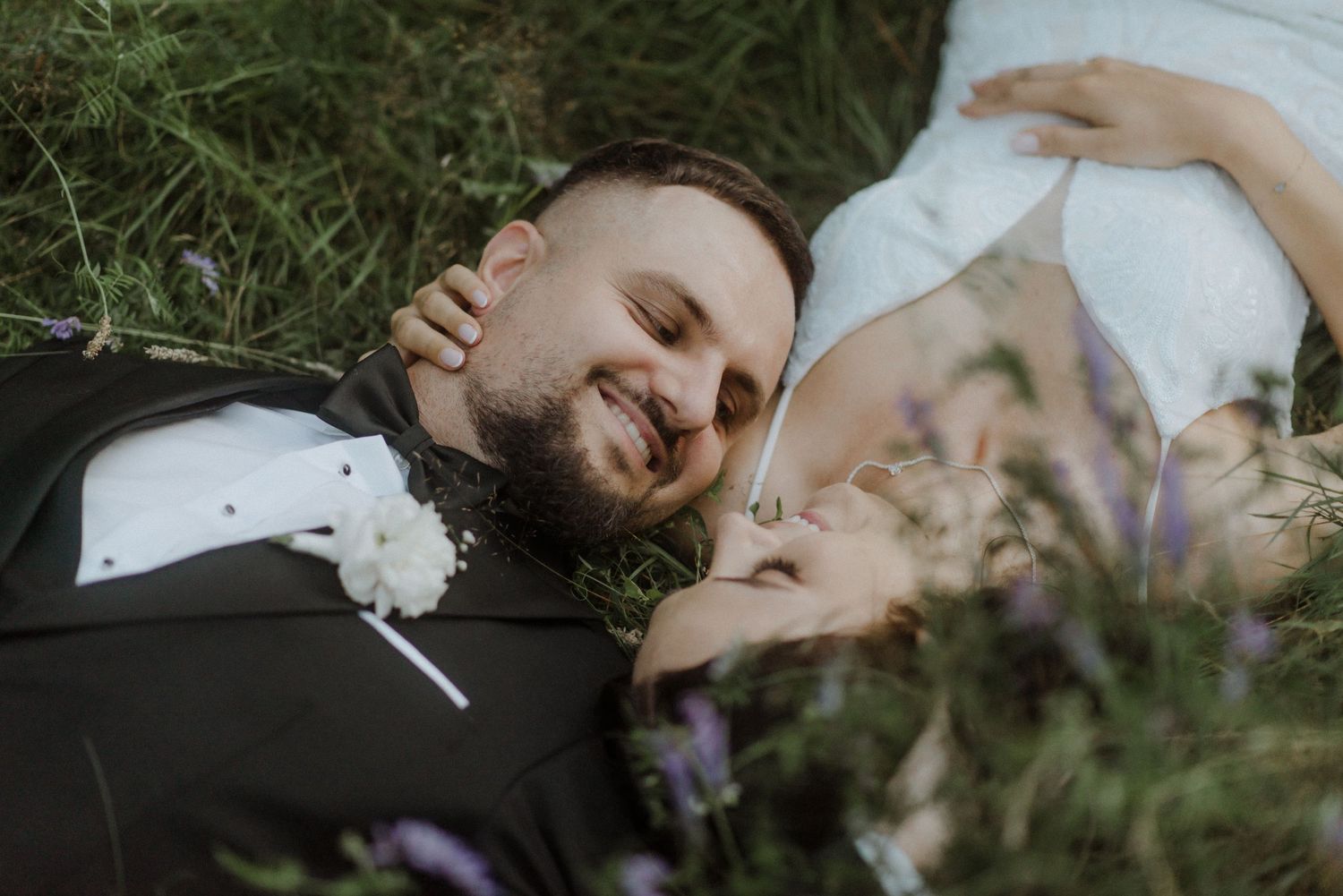 A loving couple sharing a tender moment together on grass surrounded by greenery.