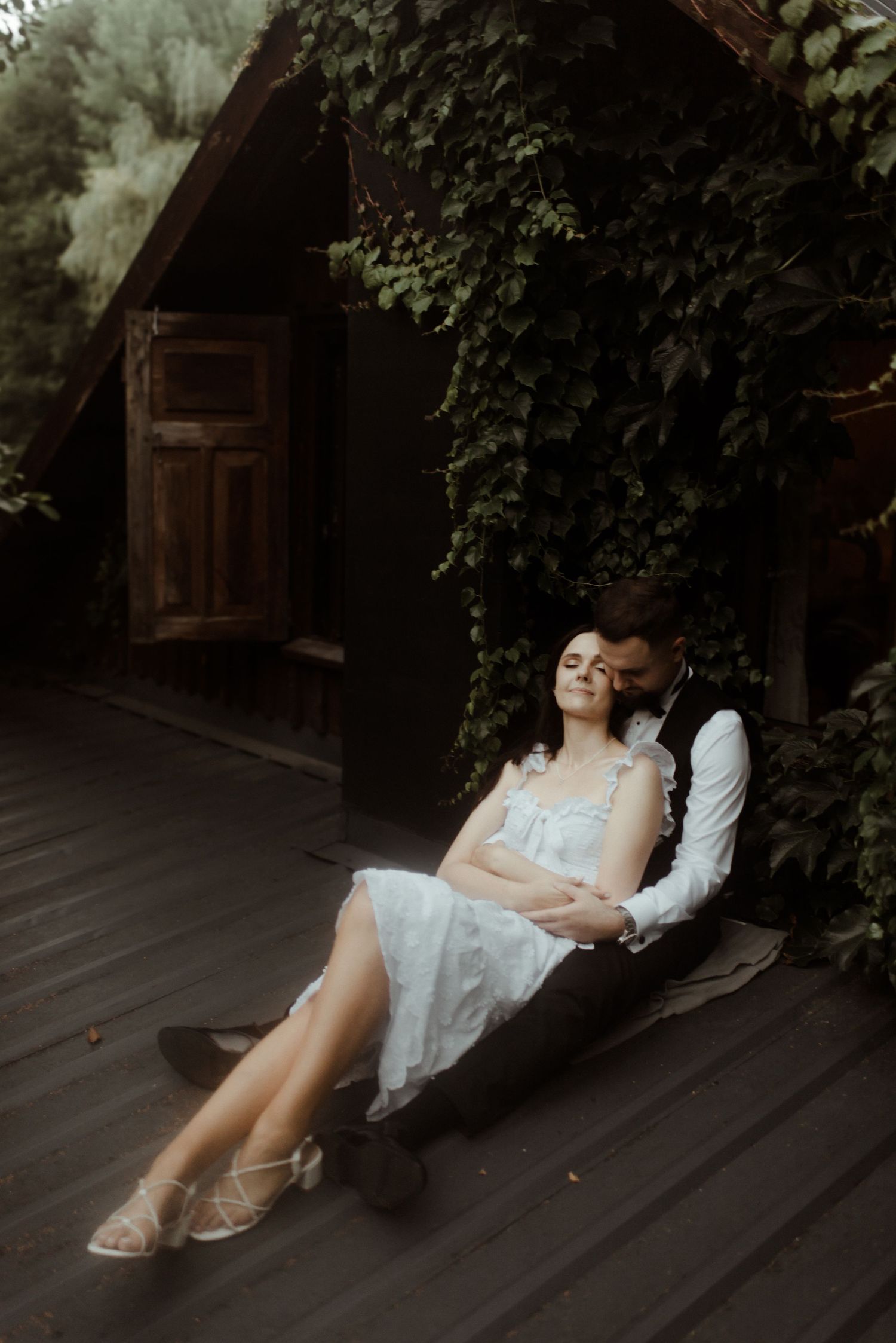 Couple relaxing on wooden porch covered in ivy and vines.
