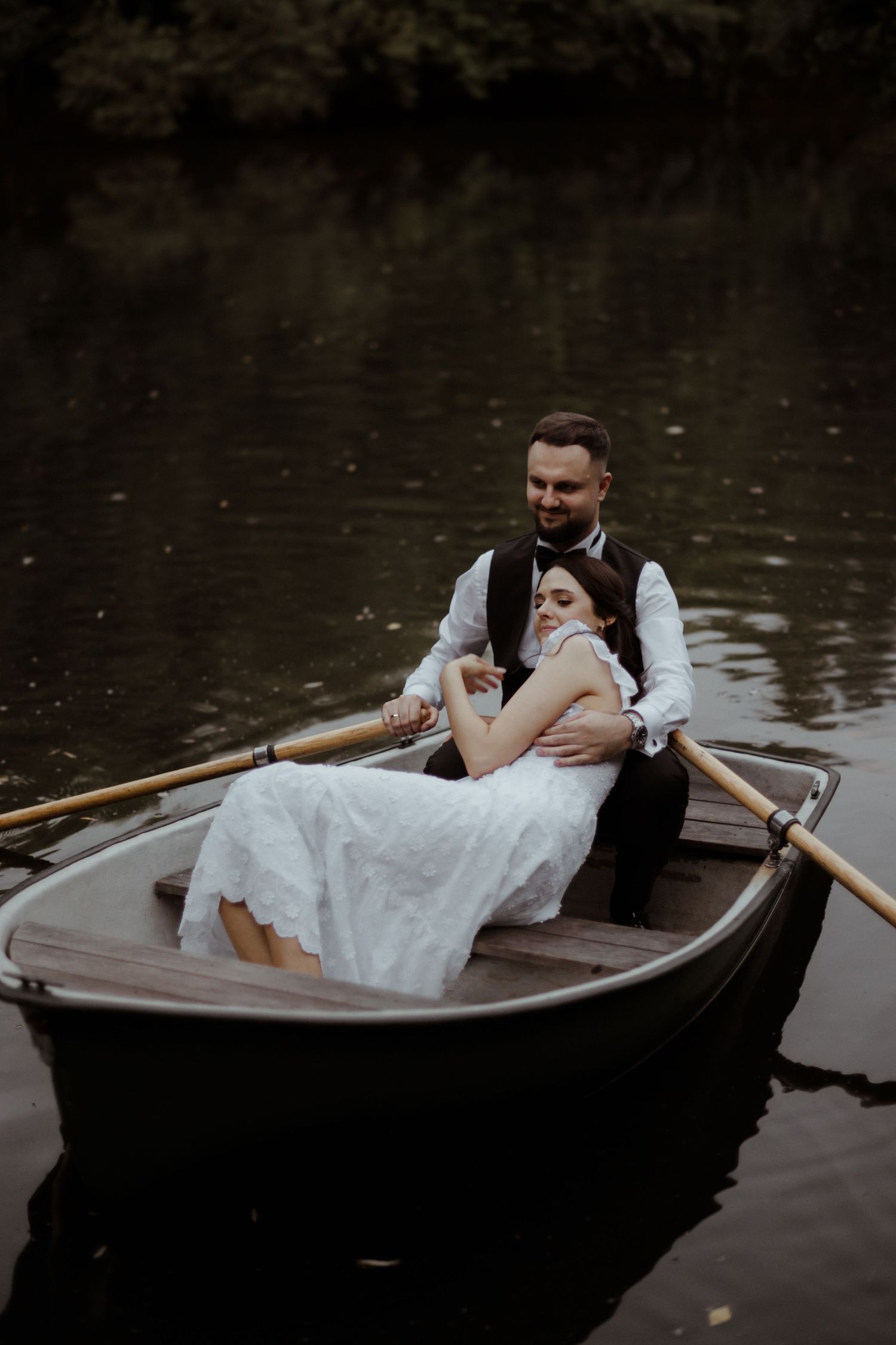 A romantic couple shares a tender moment while rowing a wooden boat on a tranquil lake.