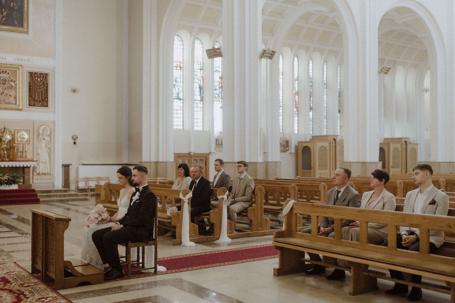 An elegant church interior with white columns and wooden pews creates a romantic atmosphere for a wedding ceremony.