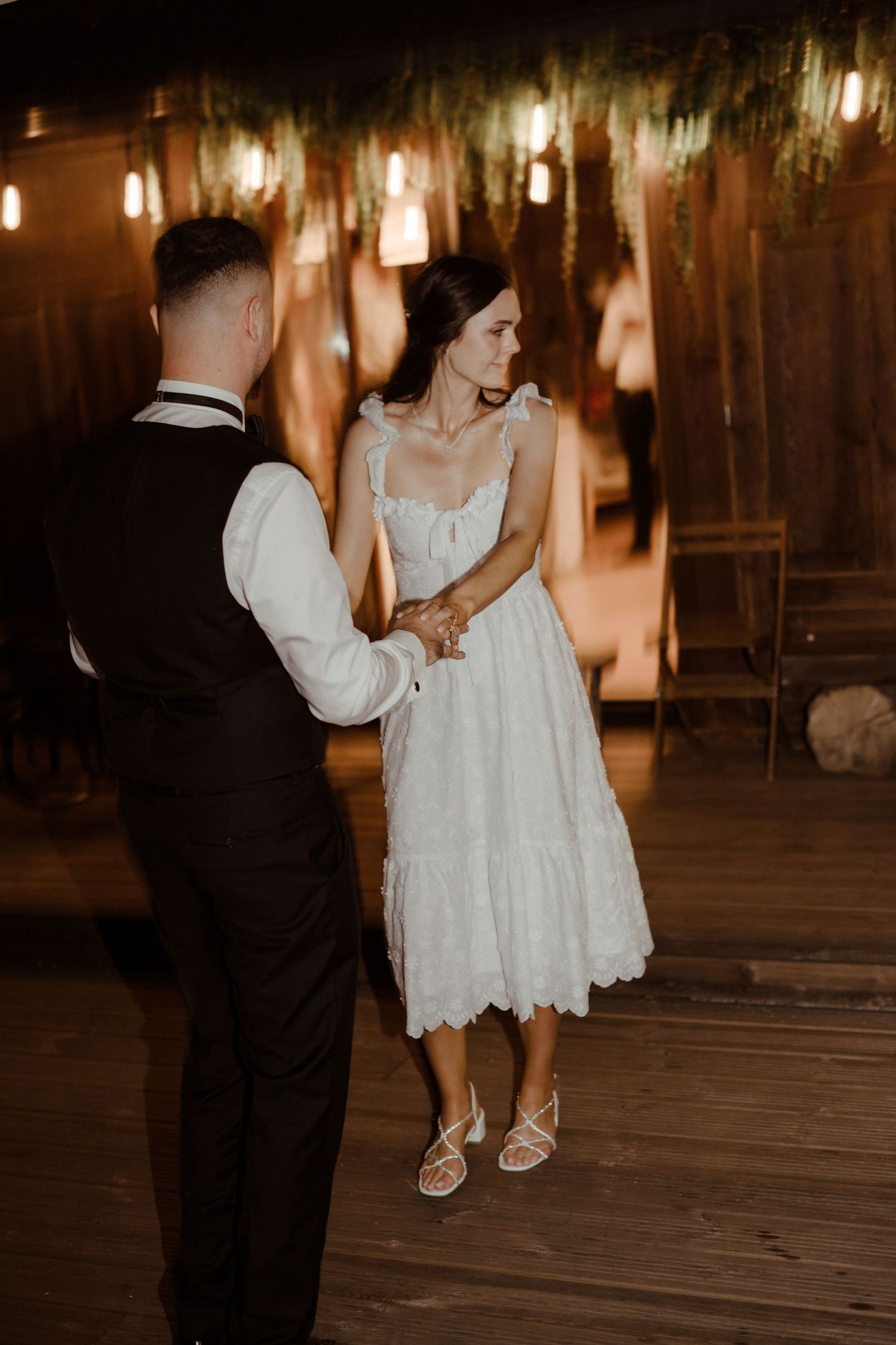 A couple shares an intimate dance moment under warm hanging lights in a rustic venue.
