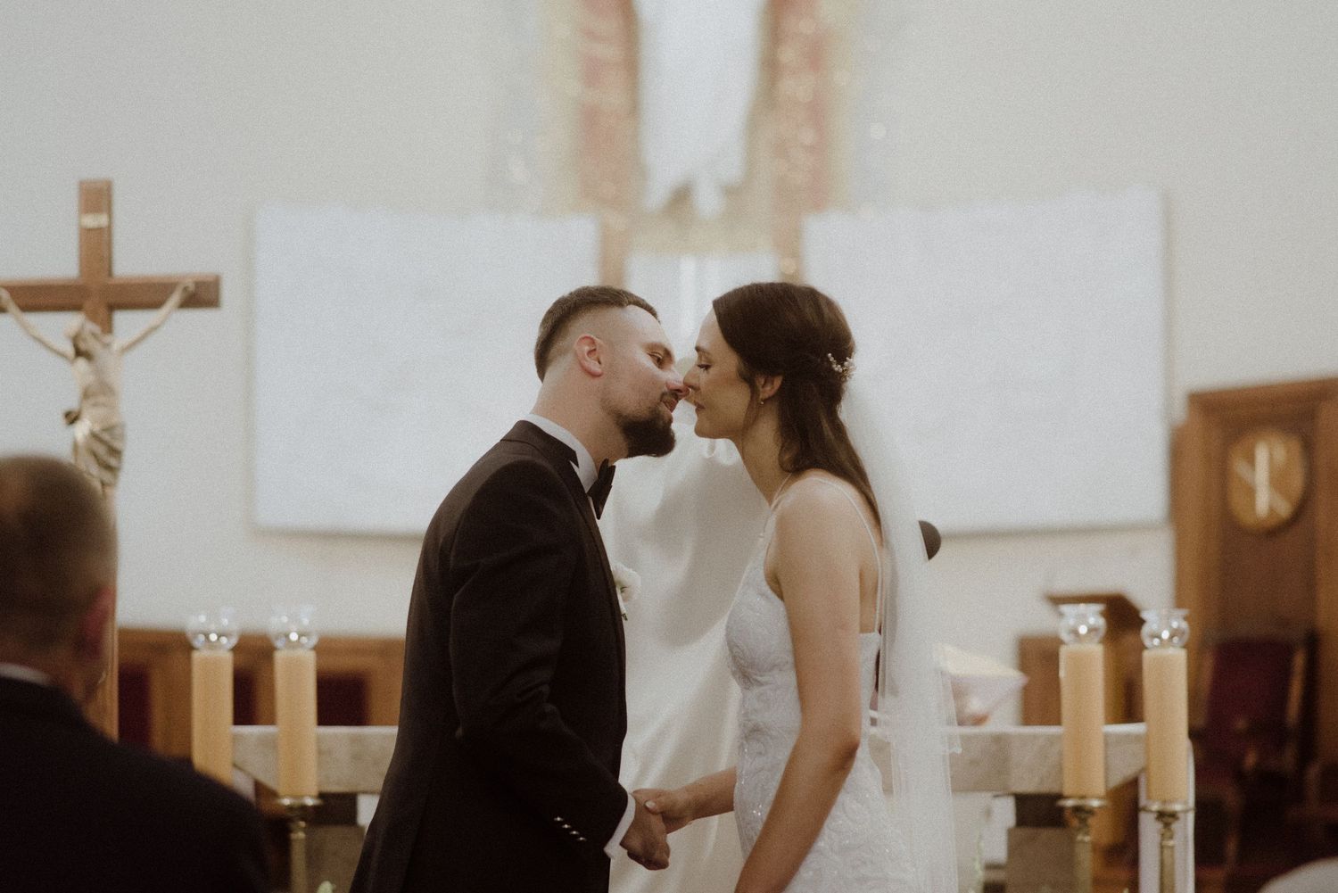 Romantic church wedding ceremony with couple at altar surrounded by white candles and floral arrangements.