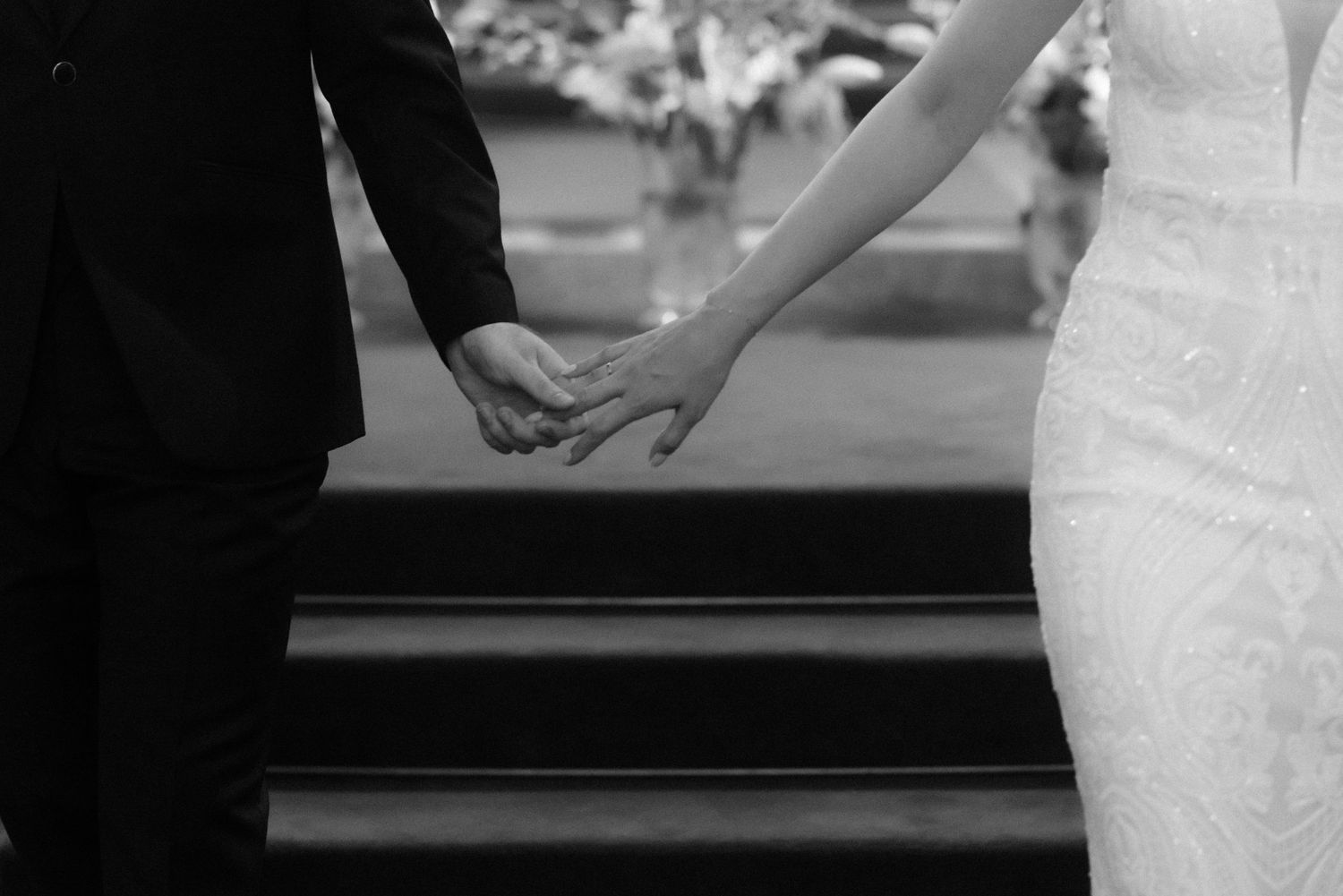 A black and white wedding photo showing a close-up view of hands holding during a ceremony.