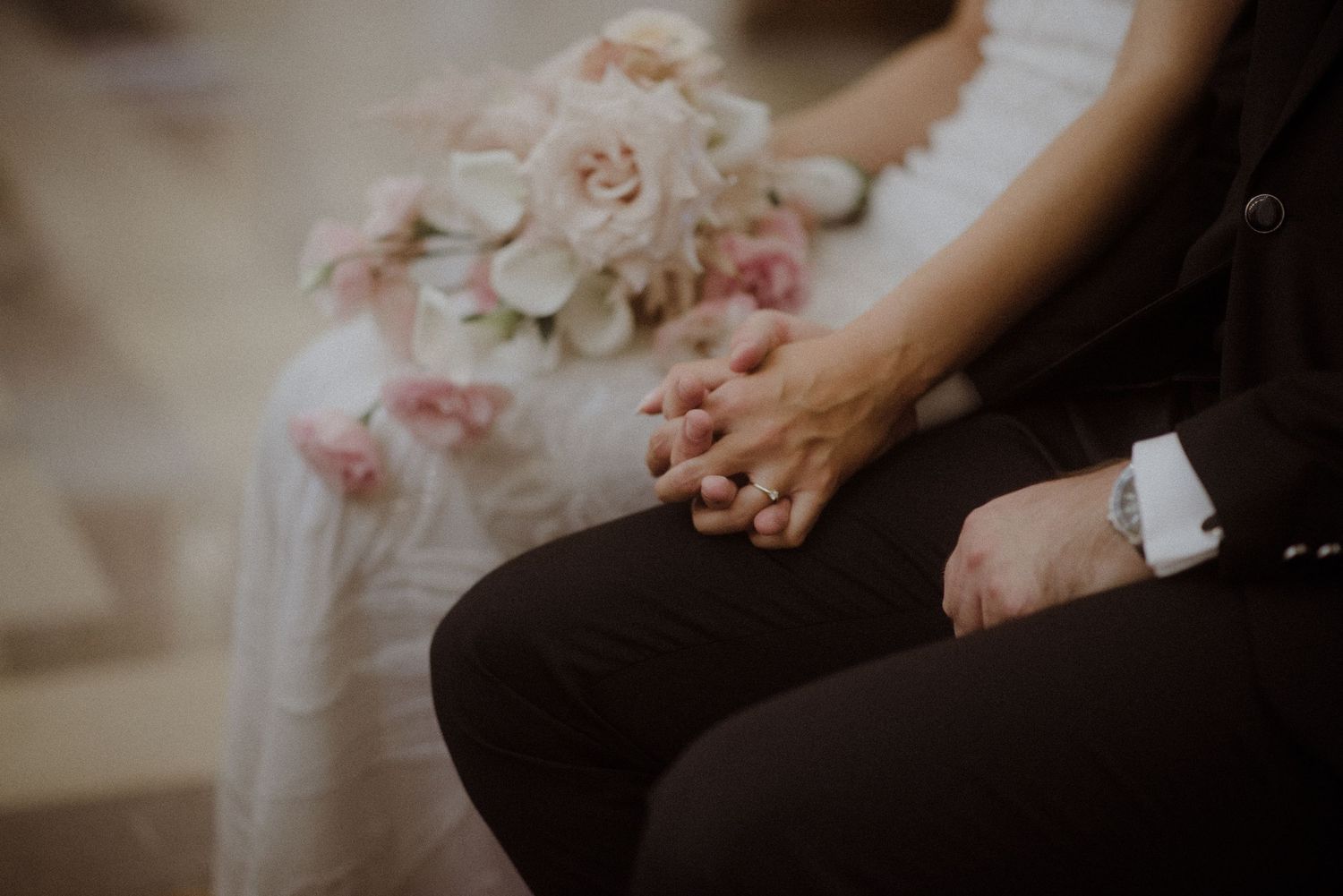 Close-up view of hands holding a delicate pink and white bridal bouquet during a wedding ceremony.