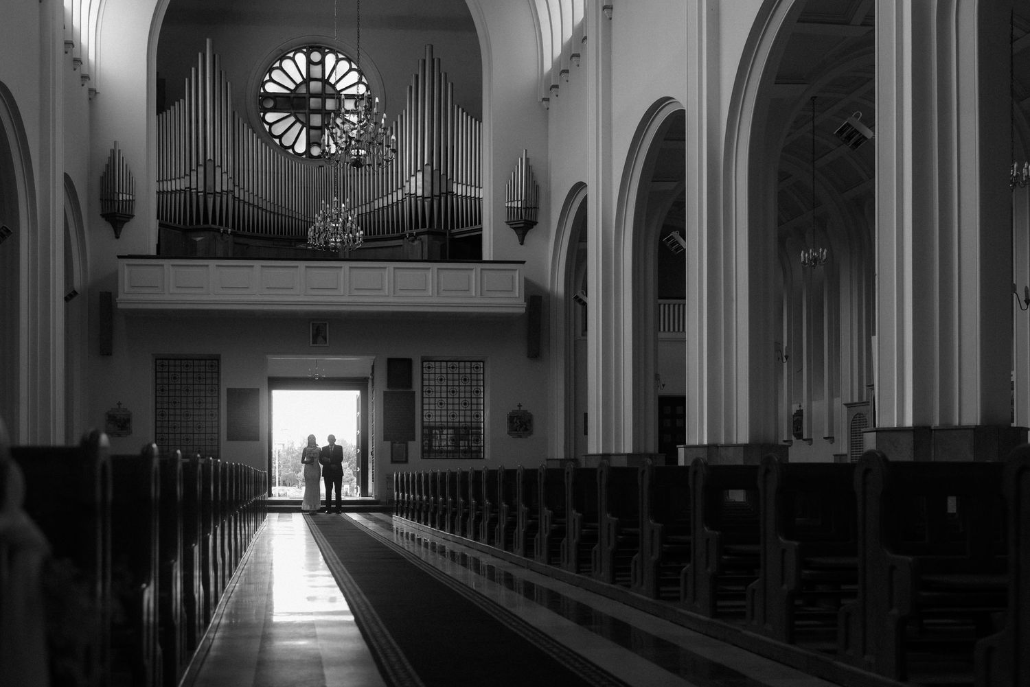 Dramatic black and white interior of church with long rows of pews leading to altar.