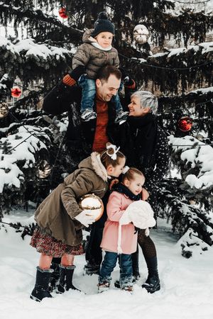 Family gathered around a snow-covered evergreen tree decorated with red ornaments.