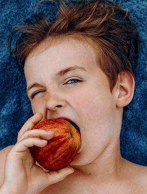 Close-up image of someone taking a bite of a fresh red apple against a blue background.