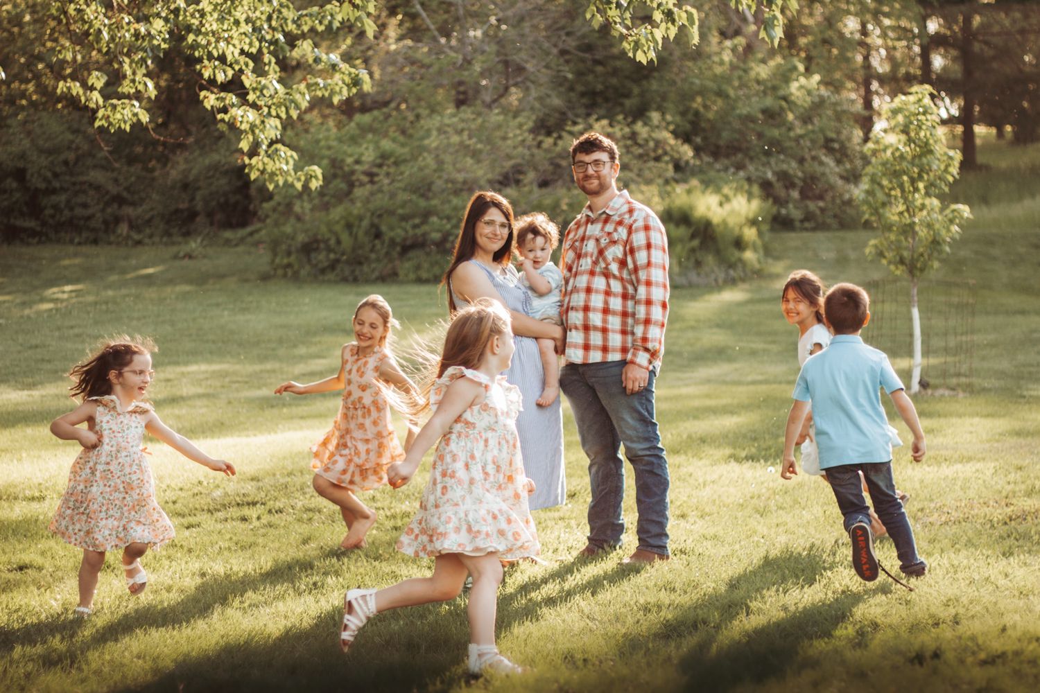 Children playing and running in sunlit grassy field during golden hour with adults watching.