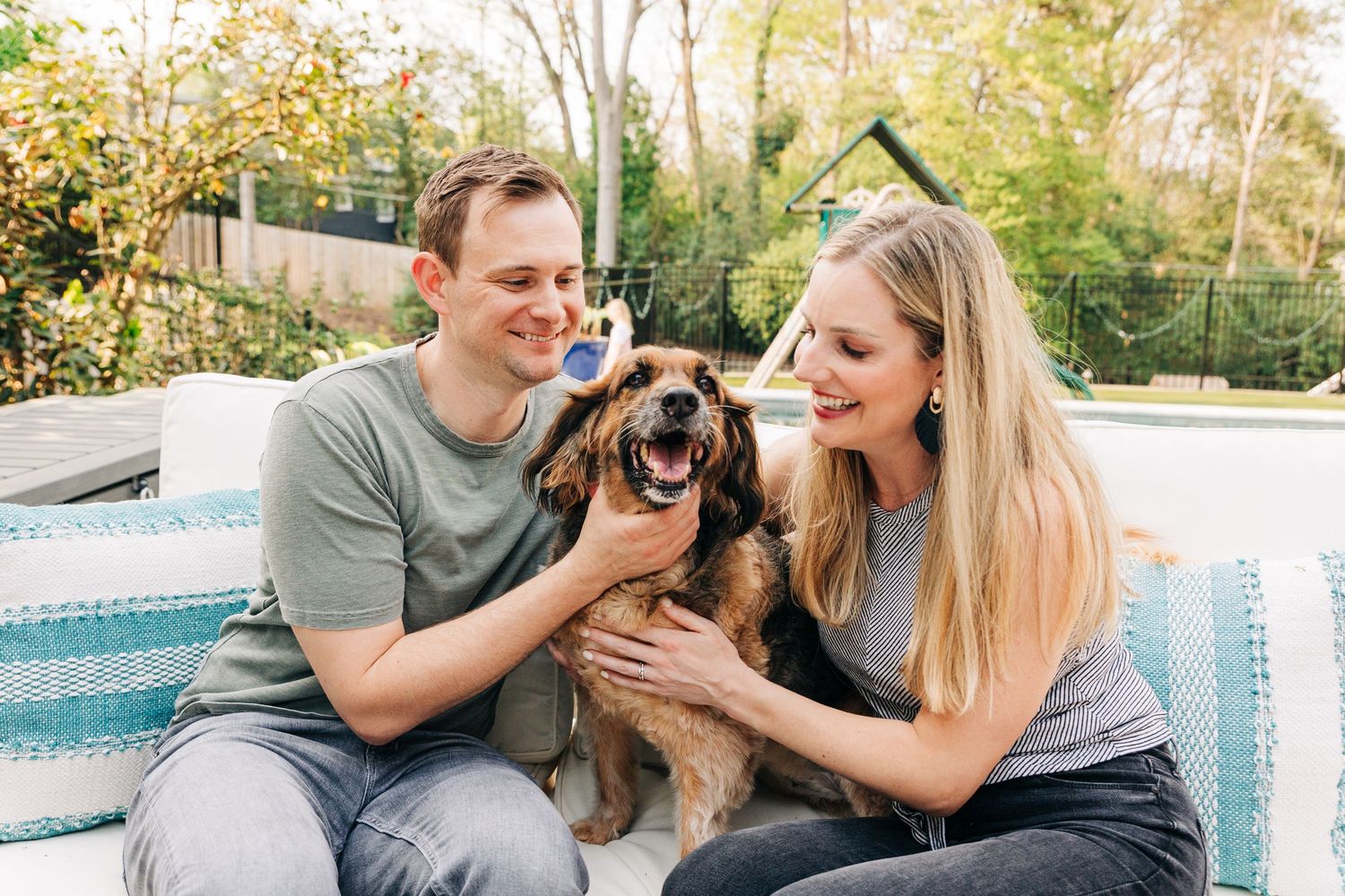 A couple enjoying quality time outdoors with their small brown dog on a sunny day.