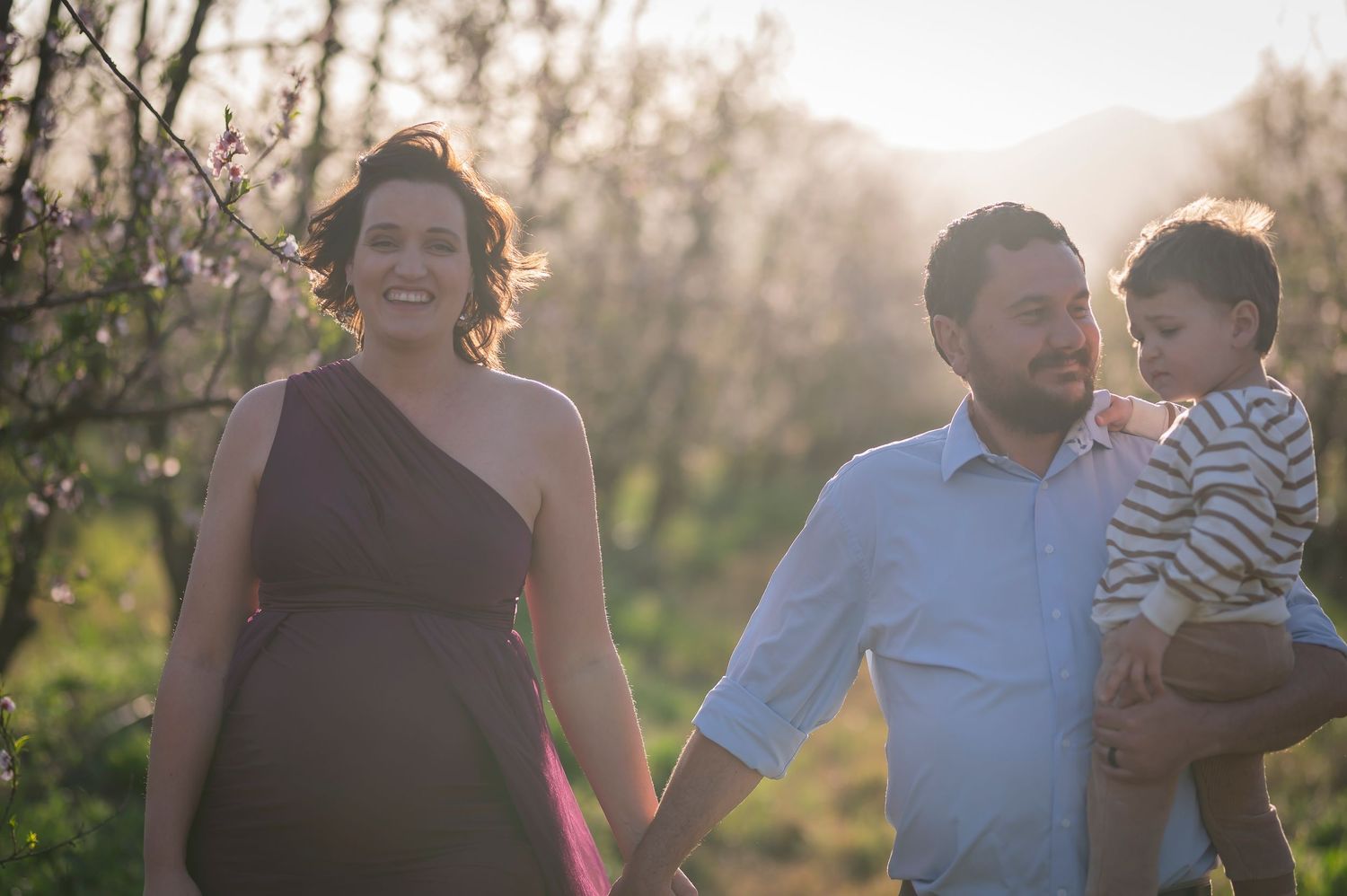 A family walks together outdoors during golden hour with spring blossoms in the background.
