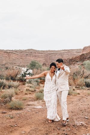 Wedding couple dancing playfully in desert landscape surrounded by red rock formations.