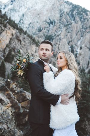 Romantic couple embracing during winter wedding shoot with snowy mountain backdrop.