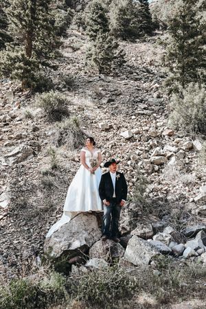 Couple in formal attire pose along rocky mountain terrain during outdoor photoshoot.