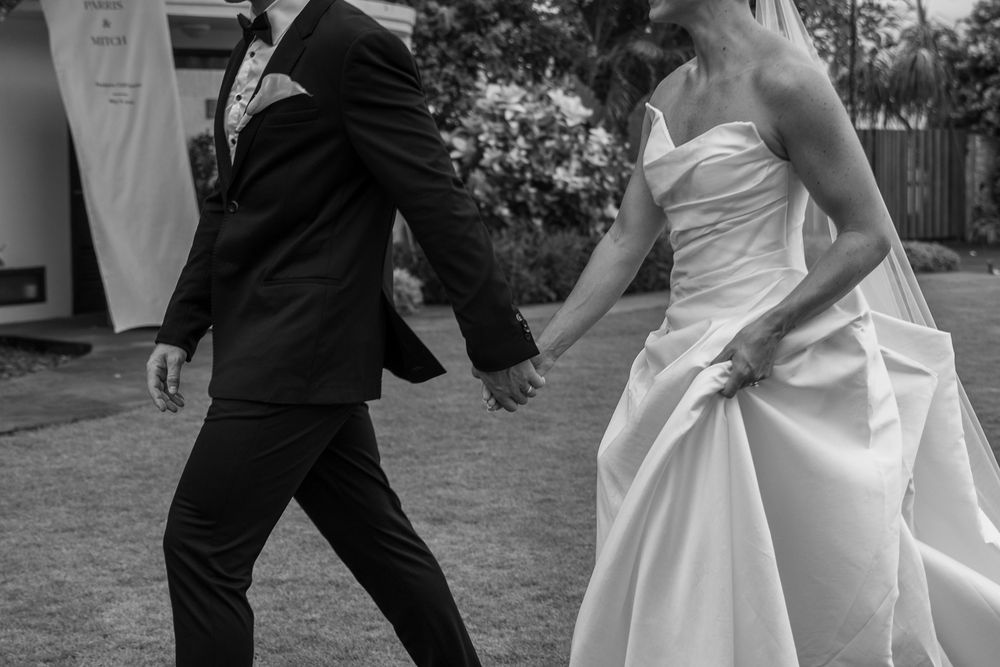 Newlywed couple playfully running and twirling across a green lawn on their wedding day.