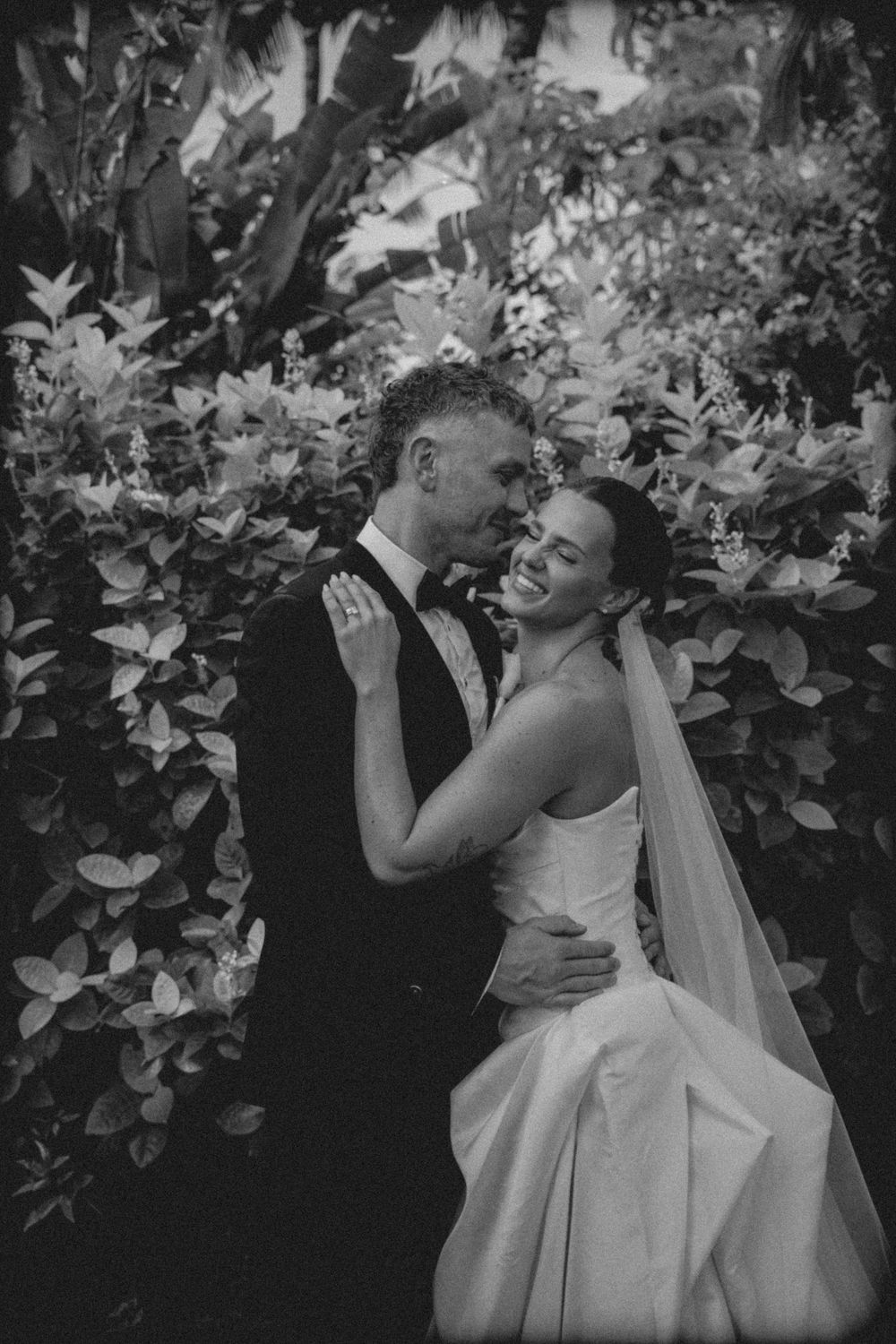 A romantic black and white photo series of a couple dancing together at an outdoor wedding reception among foliage.
