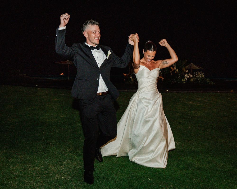 Dancing couple in formal attire make joyful moves on dark outdoor dance floor while celebrating their wedding.